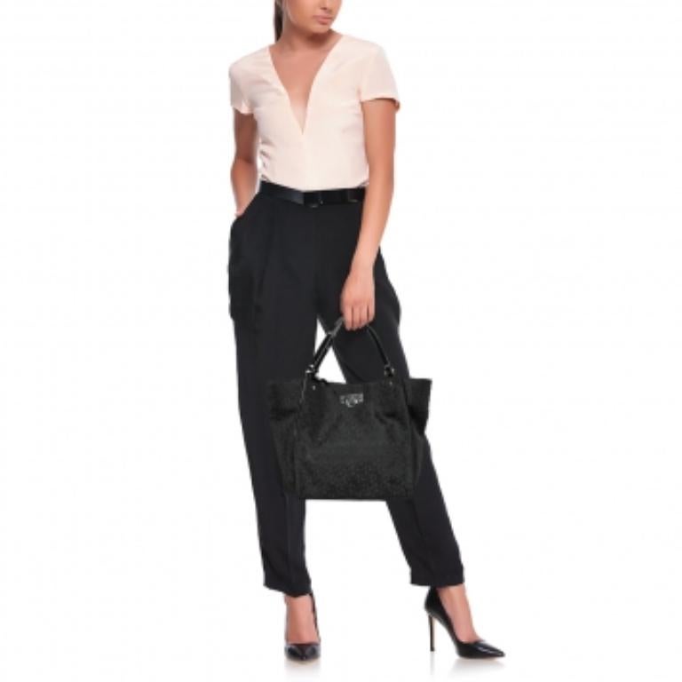 Este bolso tote de DKNY es elegante, resistente y práctico para el día a día. Está confeccionado con lona negra Monogram y charol en el exterior. Este bolso tiene dos asas, herrajes en tono bronce y un interior forrado de tela.