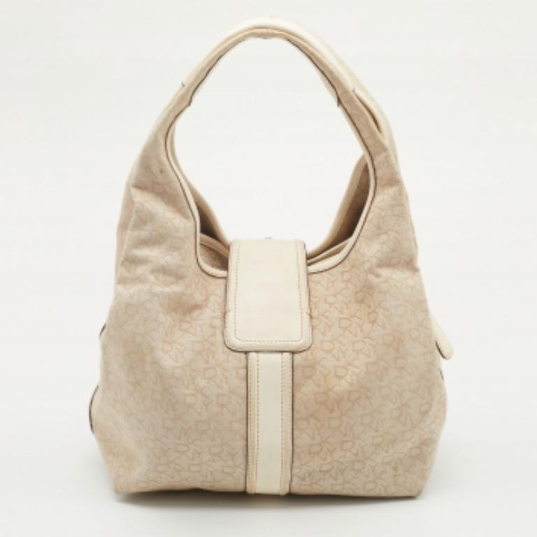 Este hobo de la Casa DKNY es ideal para el día a día. Está fabricada en lona y piel de color beige claro y crema, adornada con herrajes plateados. Presenta una caída de asa de 20 cm y está provista de un interior forrado de tela. ¡Este hobo te hará