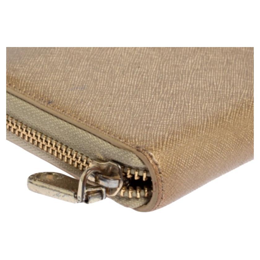 This Dkny zip-around wallet is made from metallic beige leather and has the brand logo in gold-tone metal on the front. The zipper fastening opens to reveal multiple card slots, a zip pocket, and open compartments.