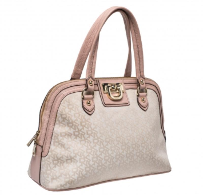 Quickly grab this dome satchel by DKNY that is crafted from pink leather and beige signature canvas. It is equipped with dual top handles, logo detailing on the front, protective metal feet at the bottom, and a zip-top closure that opens to a