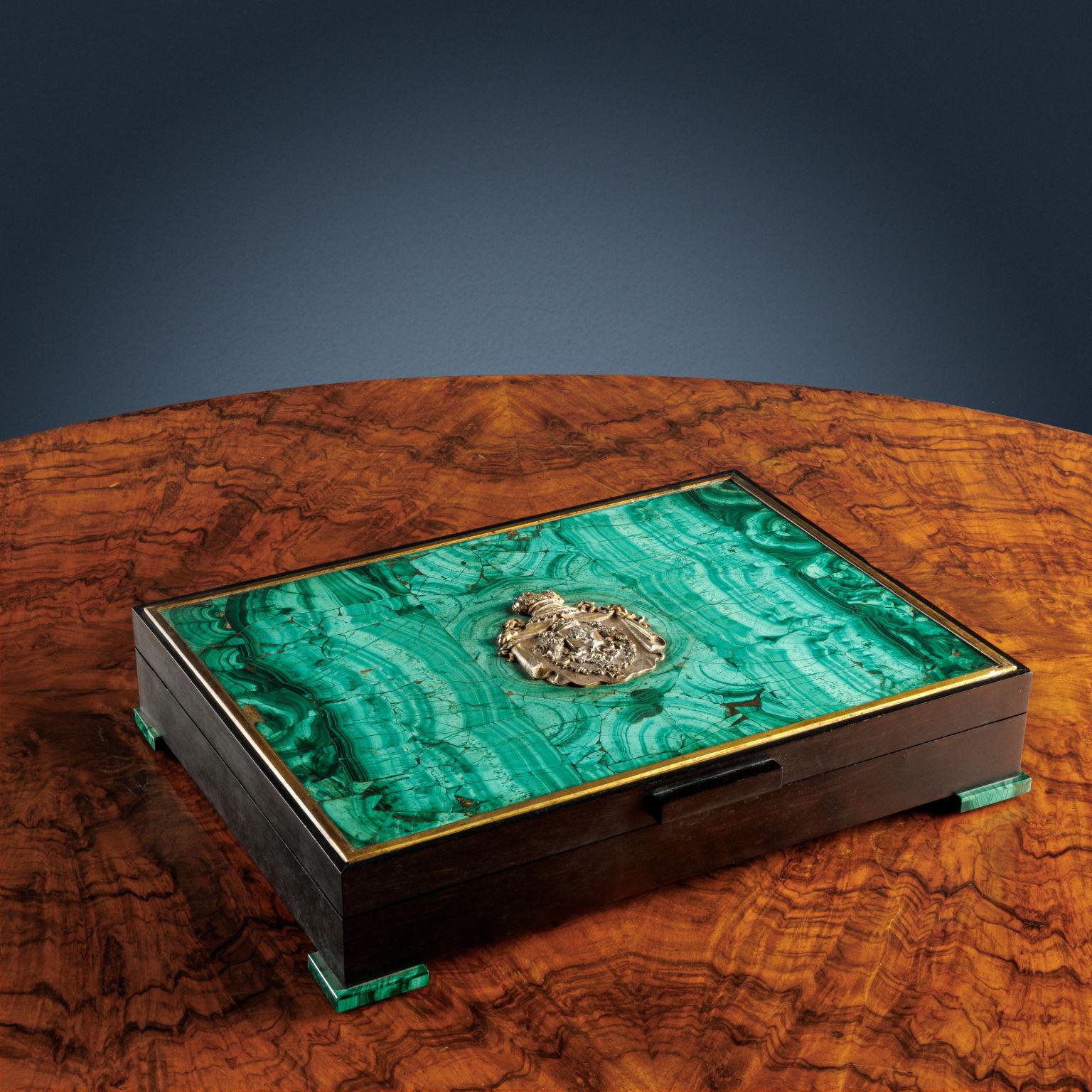 Document box made of ebony veneered wood, the top contains a malachite plate with brass border with central emblem, malachite veneered feet. The plaque in the center is in embossed and gilded sheet metal. Heraldry represents a curtain surmounted by