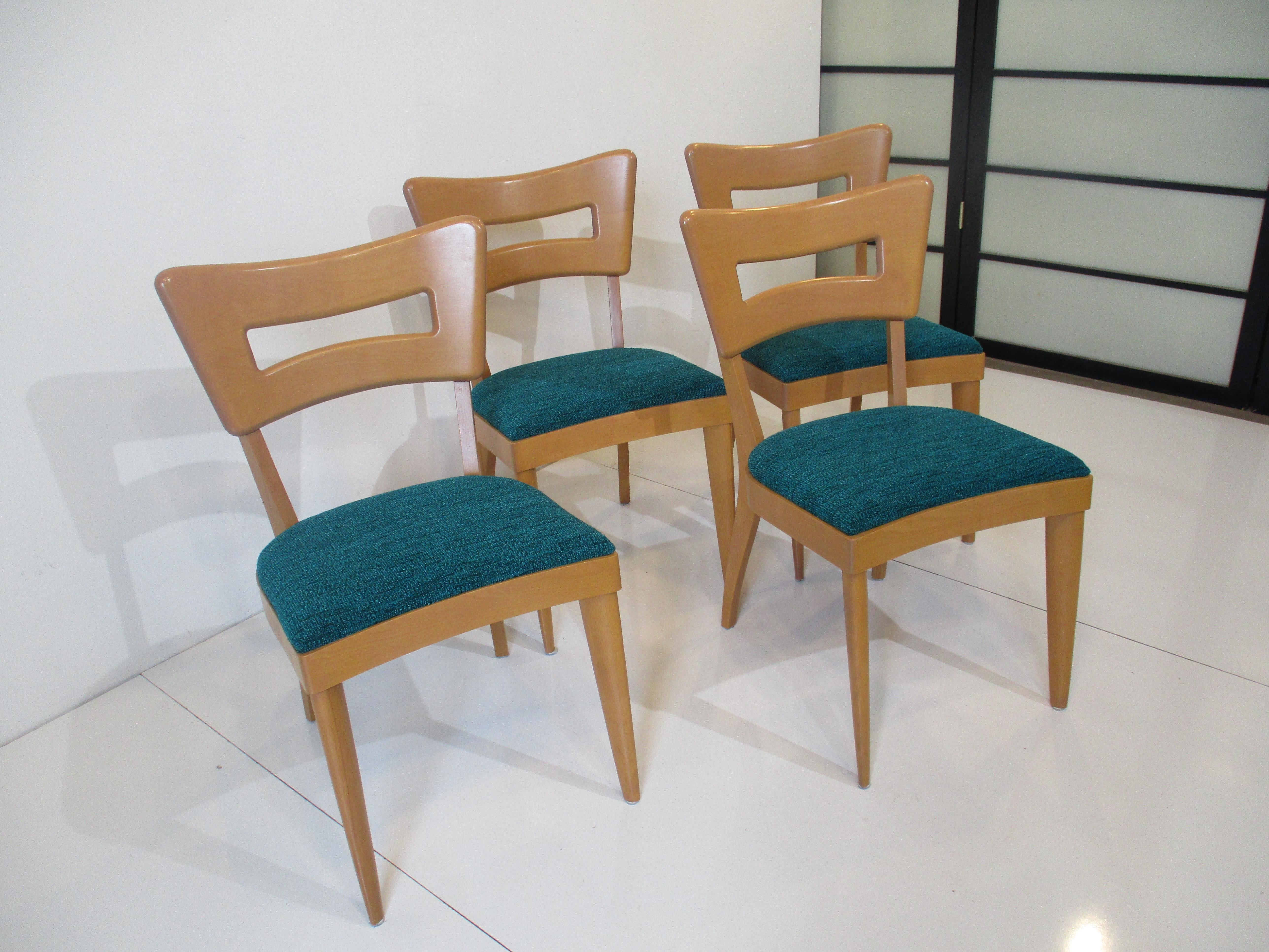 A set of four solid maple framed dining chairs known as the dog bone chair because of the sculptural backrest having the look of a dogs bone. Upholstered in a aqua fabric which is the original from the period and it looks like new. Designed by Leo
