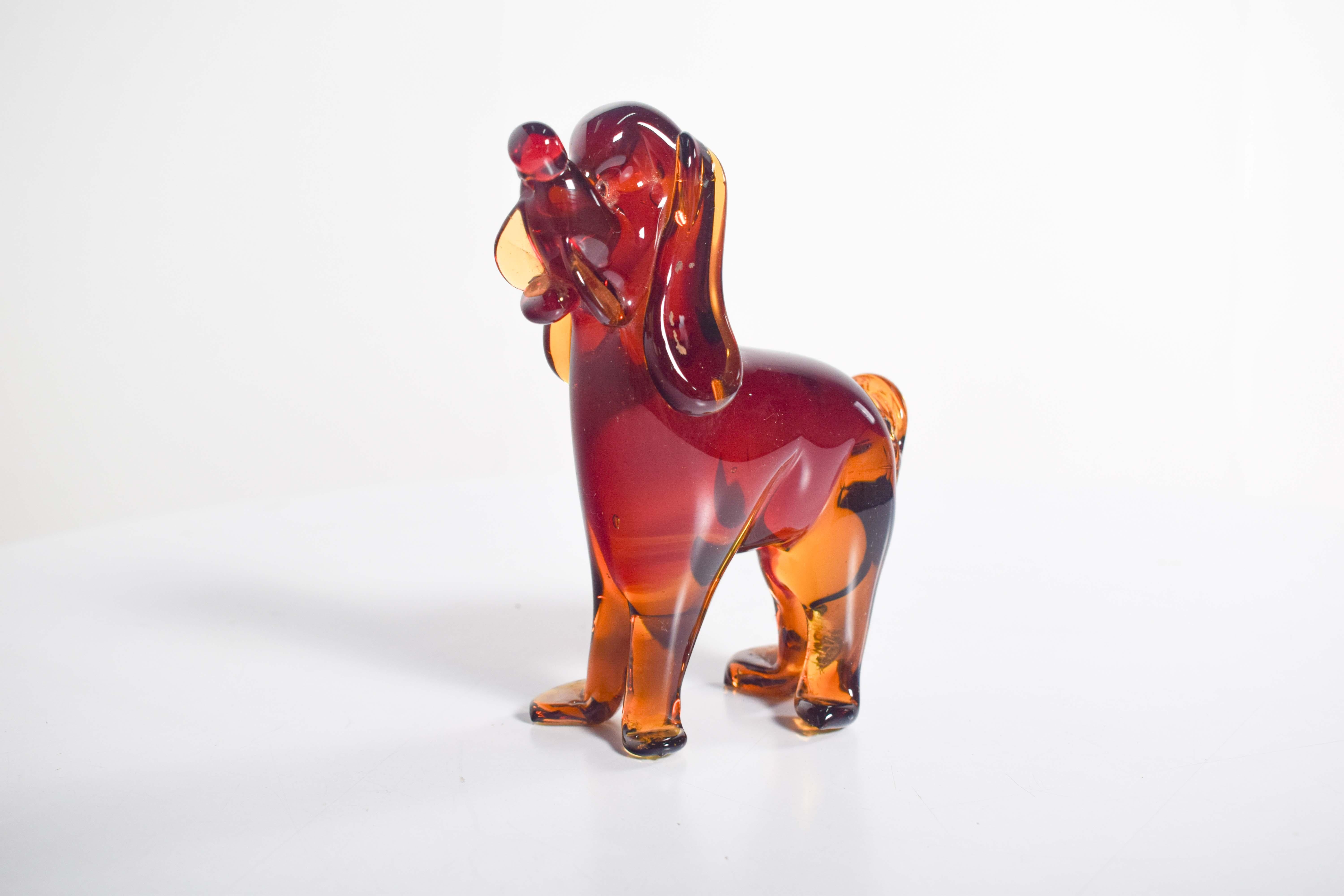 La statuetta del cane è realizzata in vetro di colore rosso e arancione, che le conferisce una presenza sorprendente e audace. Il vetro è stato sapientemente modellato per catturare l'essenza di un cane, con linee morbide e fluide che suggeriscono