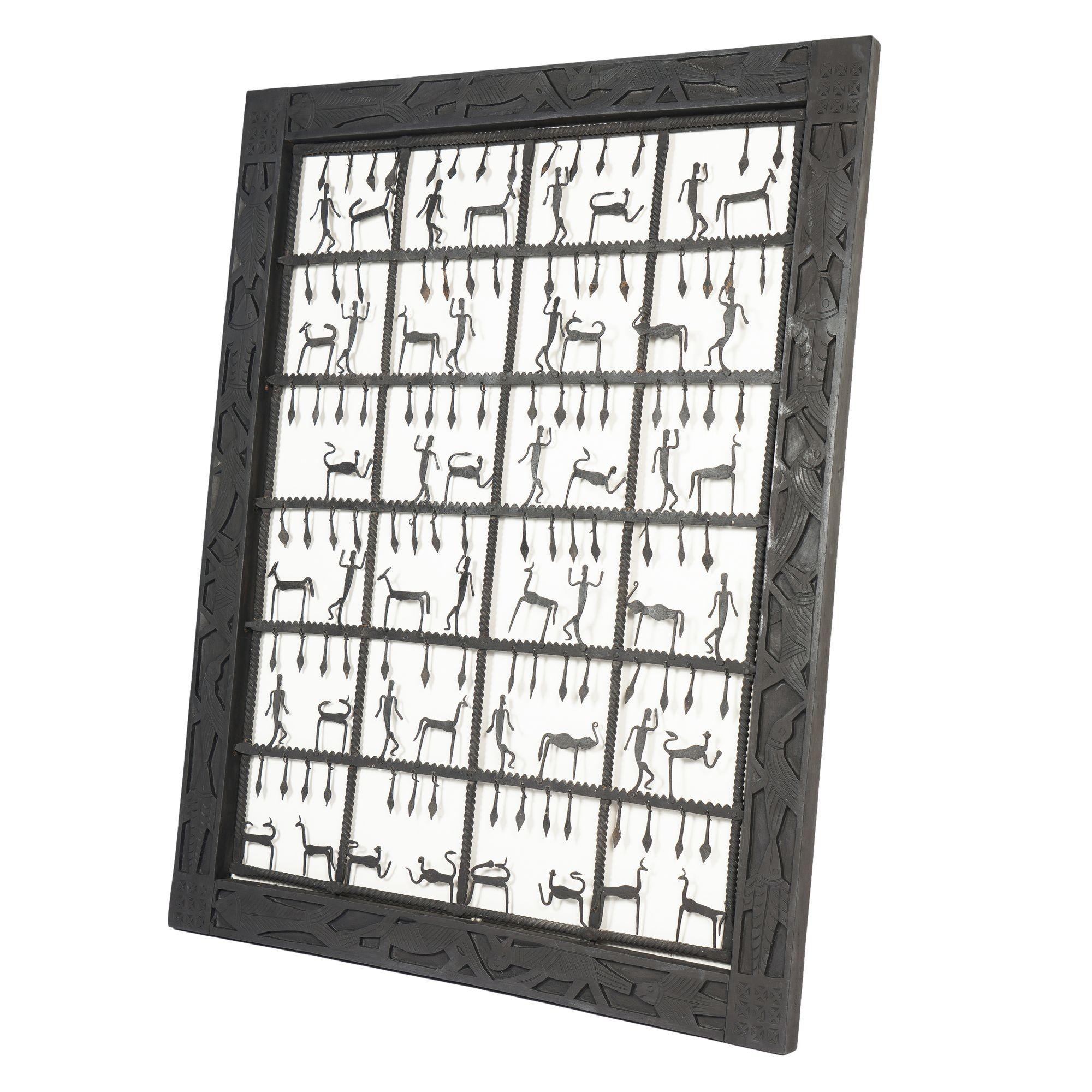 Handgeschmiedetes Dogon-Stammesgitter aus Eisen mit handgeschmiedeten Silhouetten-Figuren in einem Raster aus 24 Quadraten. Das Werk ist in seinem originalen flachen geschnitzten und bemalten Hartholzrahmen gerahmt. Der Rahmen ist mit Fischen,