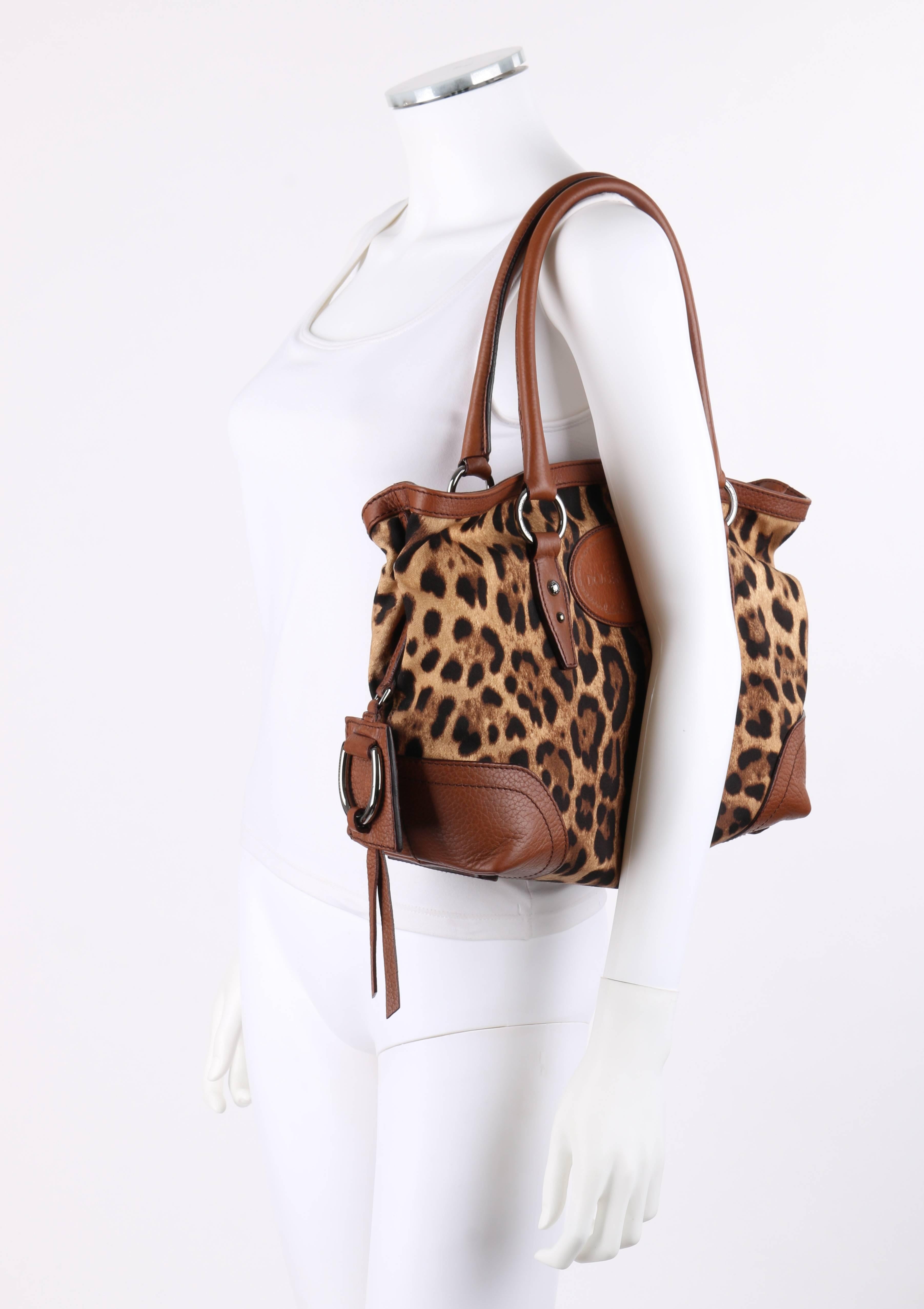 Dolce & Gabbana Animalier leopard print canvas and brown leather satchel. Dark brown and tan leopard print twill weave canvas exterior. Brown pebbled leather binding at opening and applique at corners. Two single rolled leather handles attached via