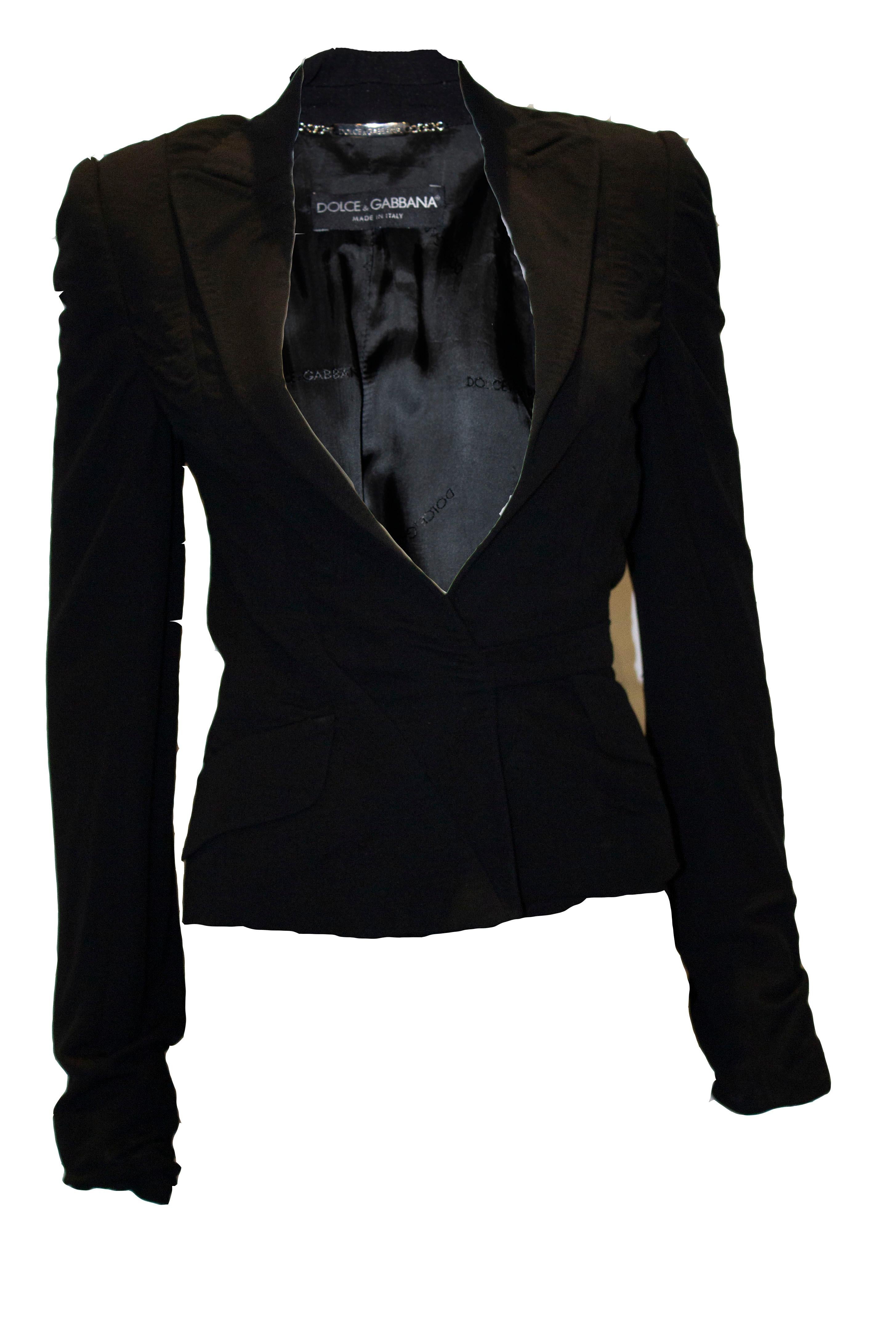 A chic blck jacket by Dolce and Gabanna. The jacket ahas two faux pocket flaps and an uusual wrap around tie belt. It is a rayon, nylon and spandex mix.