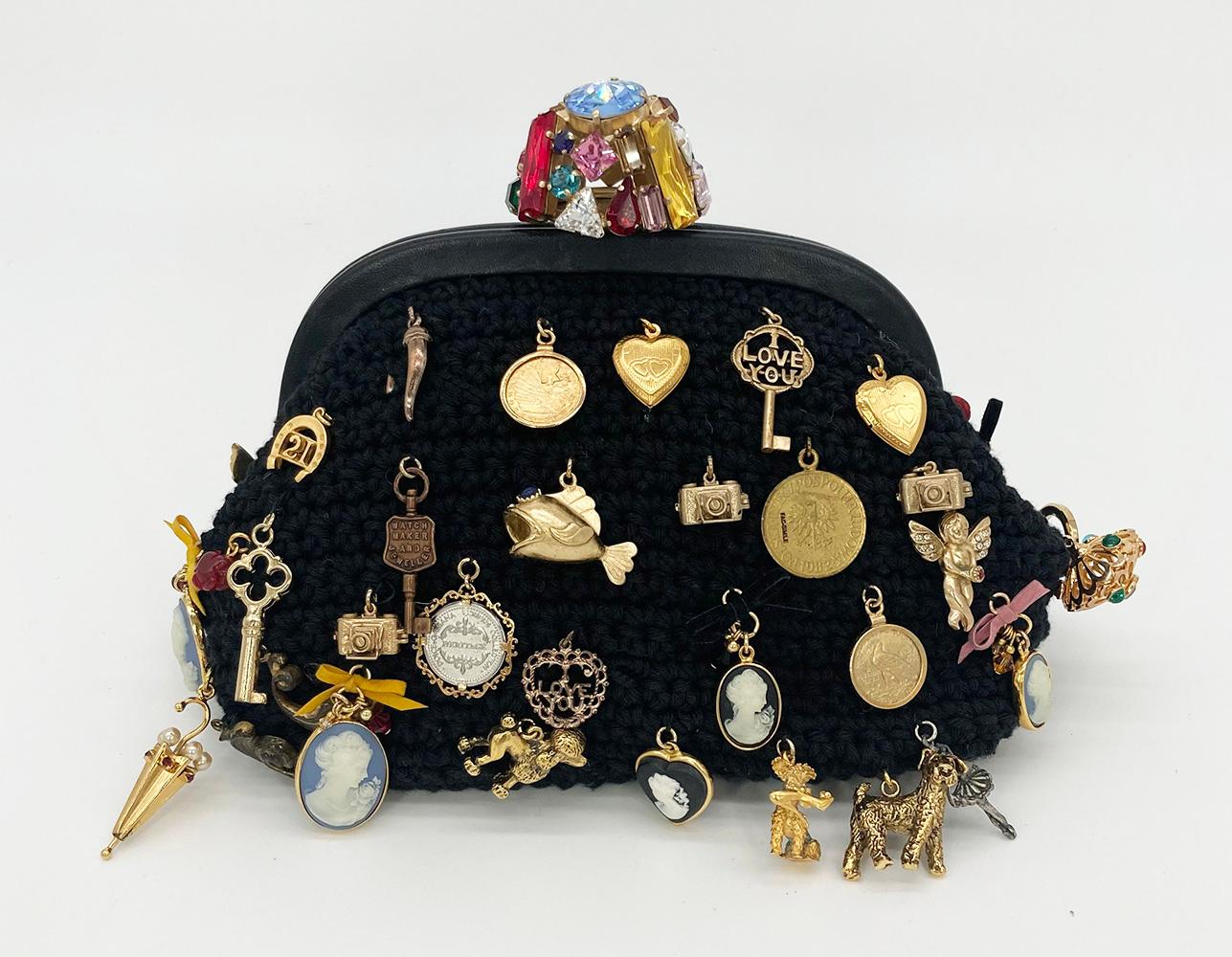 Rare and amazing Dolce and Gabbana black wool knit charm clutch in excellent condition. Black knit wool exterior trimmed with black leather edges and various multi tonal charms along front side. Top multicolored gemstone closure lifts to reveal a