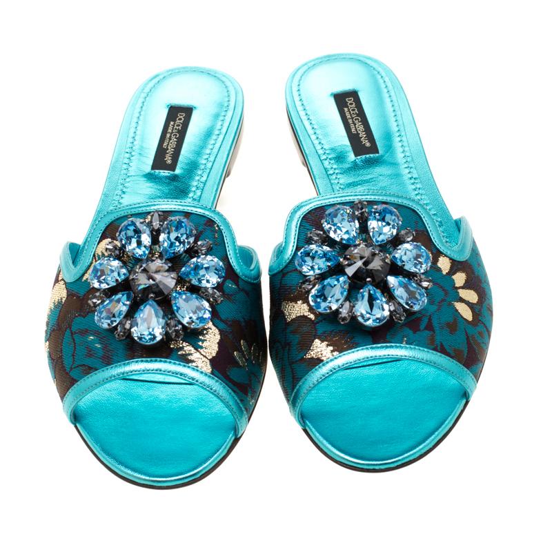 Slip on in these glamorous slides from Dolce and Gabbana! Crafted in blue brocade fabric and leather, these slides are embellished black-tone floral embellishment on the vamp. The Italian made beauties have soft leather-lined insoles. Ideal to
