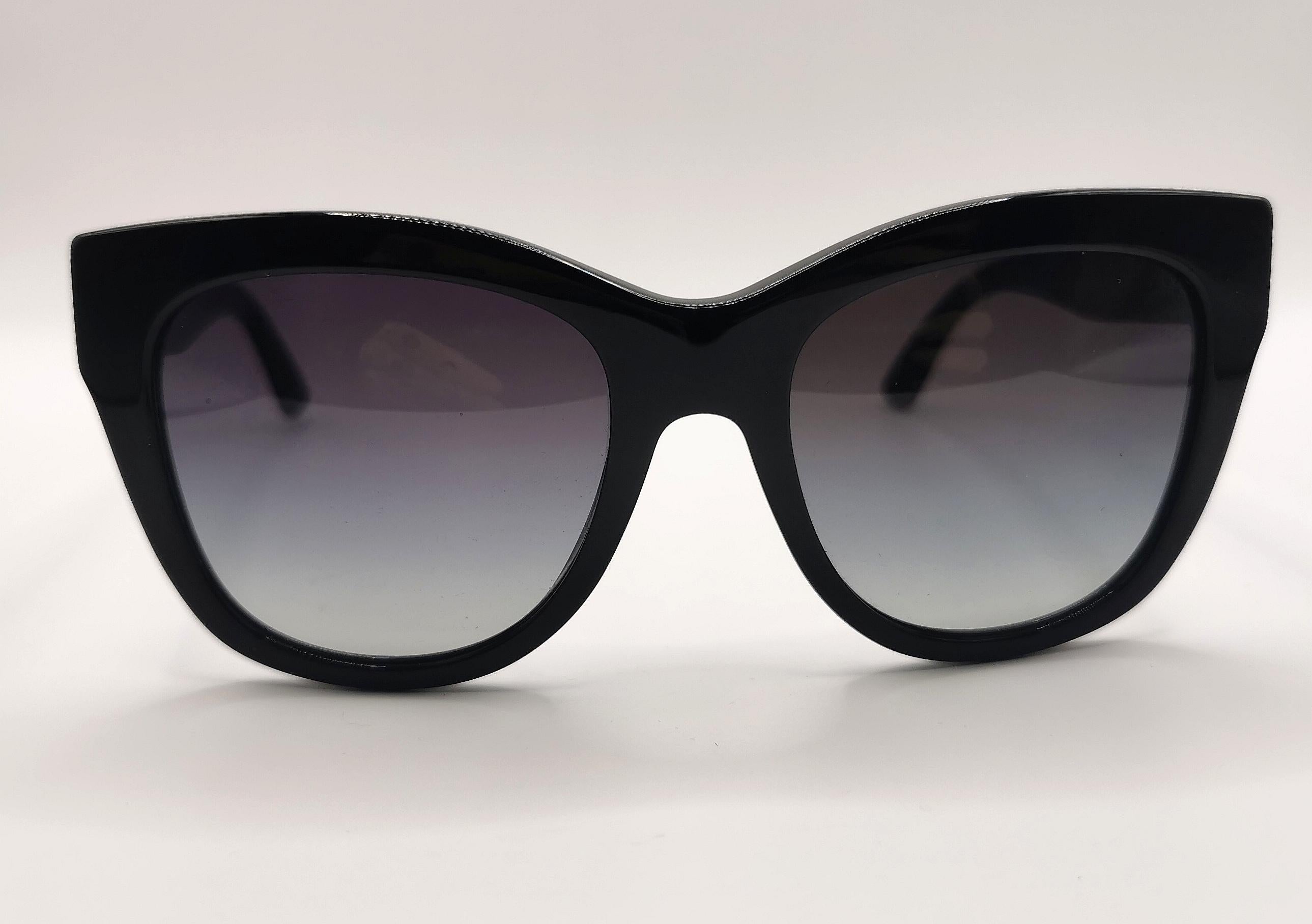 Une paire de lunettes de soleil Dolce and Gabbana très élégante.

Elles sont dotées d'une épaisse monture en acétate noir et de lentilles noires dégradées. Les lentilles sont larges et ont un léger effet œil de chat à l'extrémité.

Un logo Dolce and