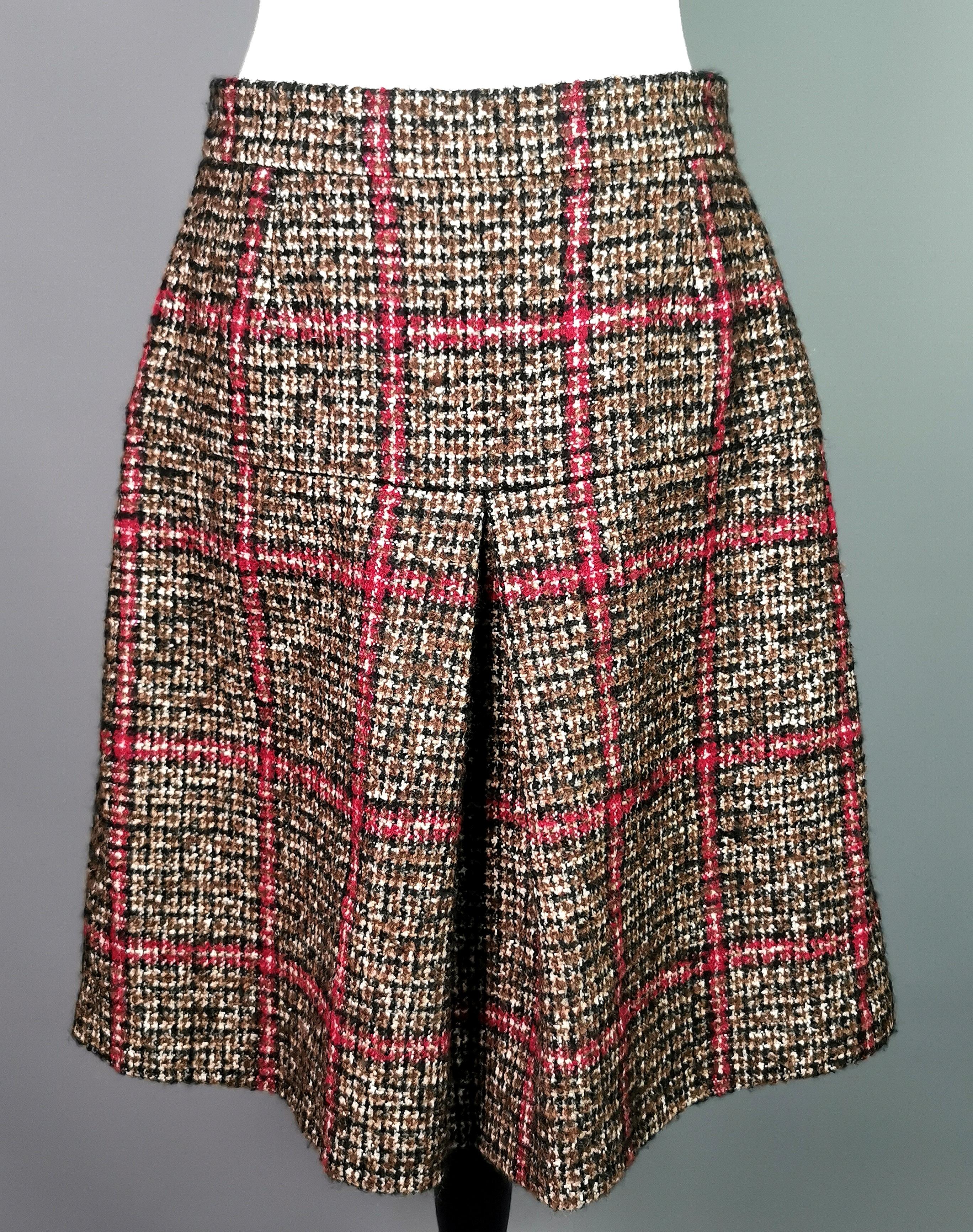 A stylish Dolce and Gabbana Tweed pleat front skirt.

A line style with a deep front pleat in a brown, white and red check wool blend.

Zip and snap fastening to the back, the skirt has an awesome silky animal print lining.

There are multiple ways