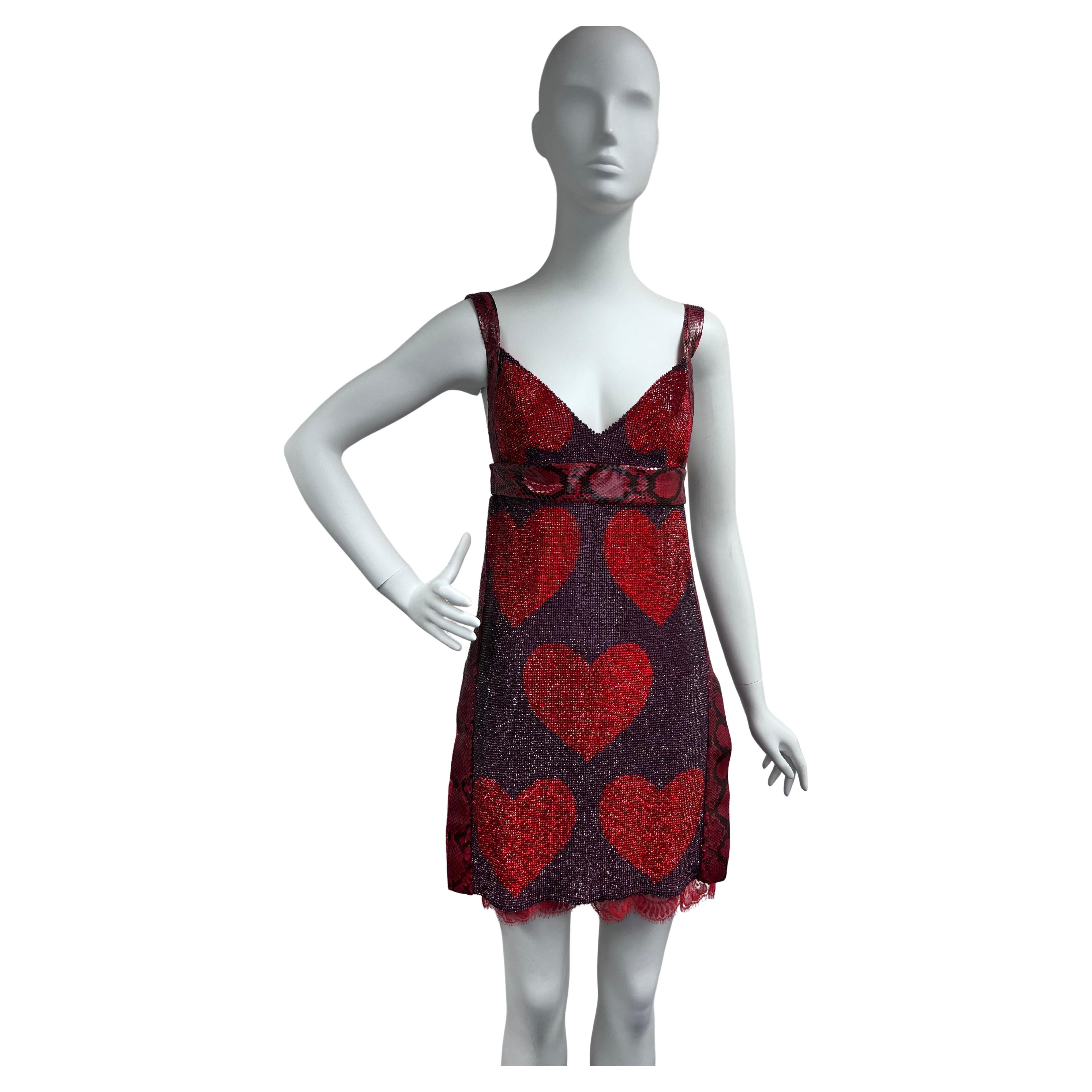 A bold and captivating statement piece, this Dolce & Gabbana mini dress is a fusion of glamour and edge. The dress features a sheer mesh base lavishly adorned with shimmering red crystal hearts, creating a striking contrast against the deep purple