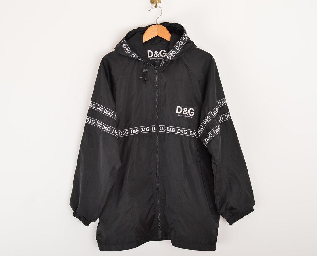 1990's DOLCE & GABBANA black hooded nylon jacket, featuring taped 'D&G' spellout to the front and reverse. 
 
Features;
x2 Front hip pockets
Central line zip fasten
Elasticated cuffs
Piece No 126-3004
100% Nylon
 
Sizing;
Pit to Pit; 26''
Pit to