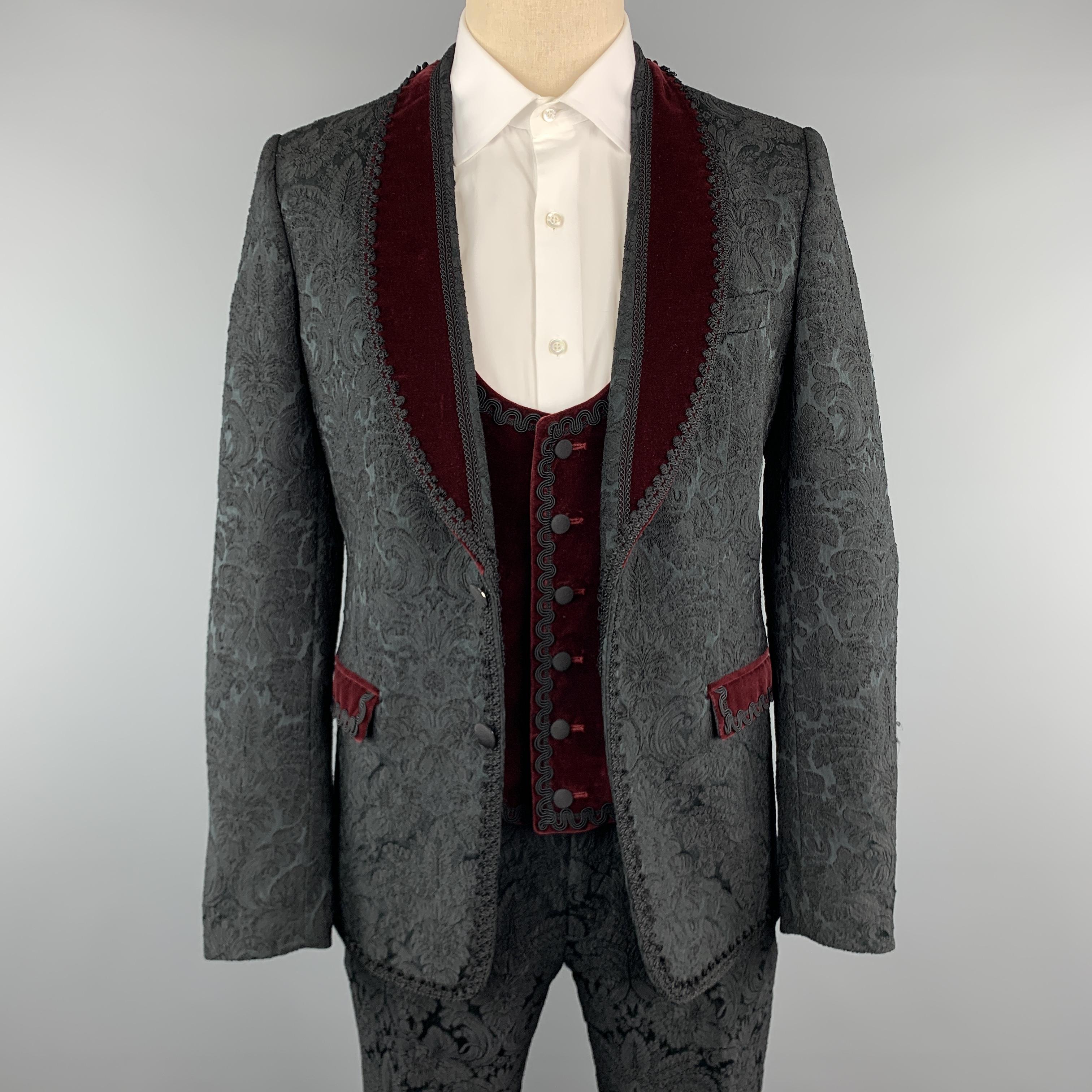 DOLCE & GABBANA three piece suit comes in black brocade fabric and includes a single breasted, two button dinner jacket with a burgundy velvet shawl collar, double vented back, and lace trim with a matching velvet vest and slim cut trousers. Made in