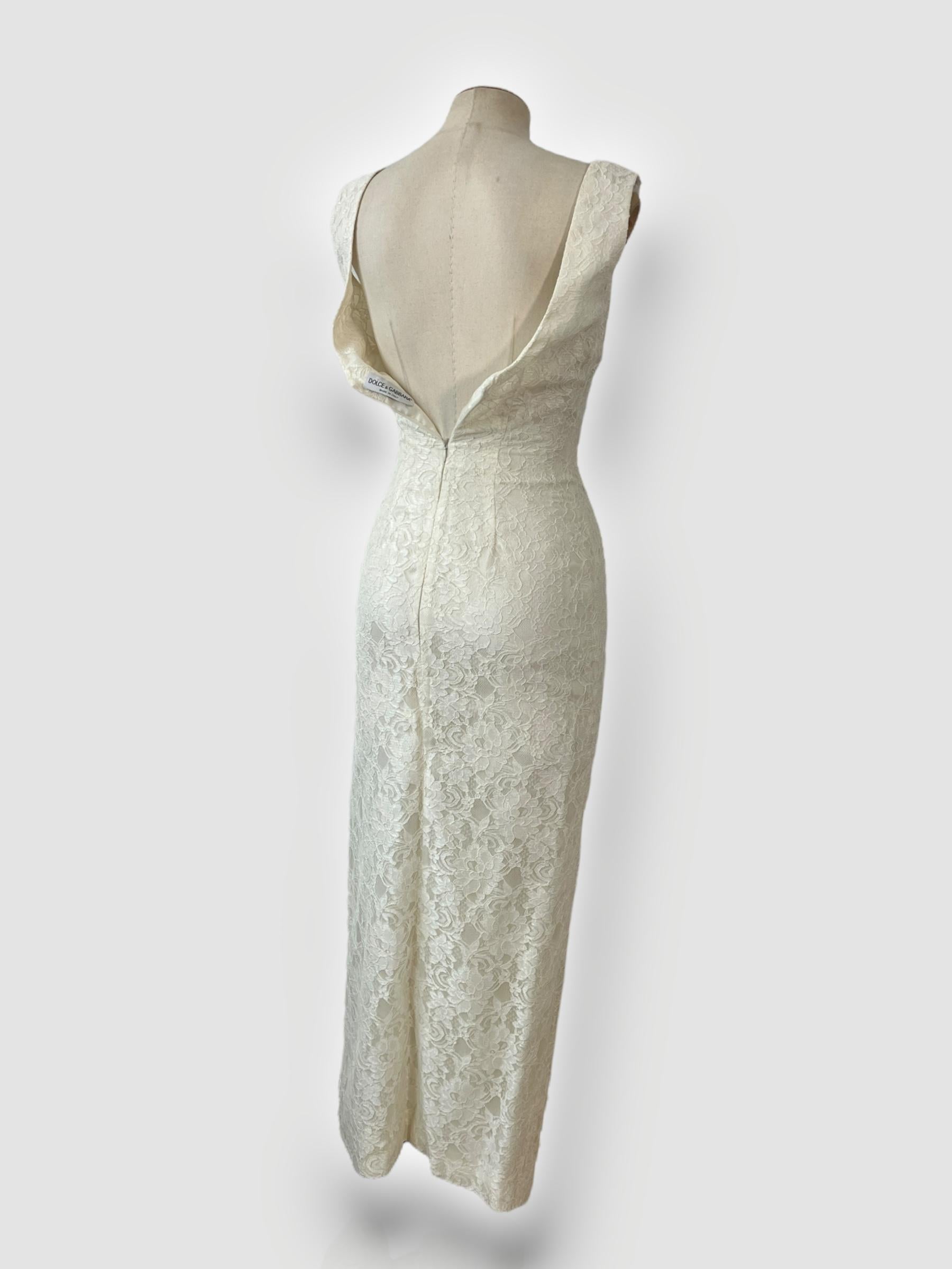 

Piece Description: This stunning 90s Dolce & Gabbana ceremony dress is crafted from delicate lace, exuding timeless elegance. Designed to flow to the floor, it features a graceful silhouette with a low back that adds a sensual touch. The back