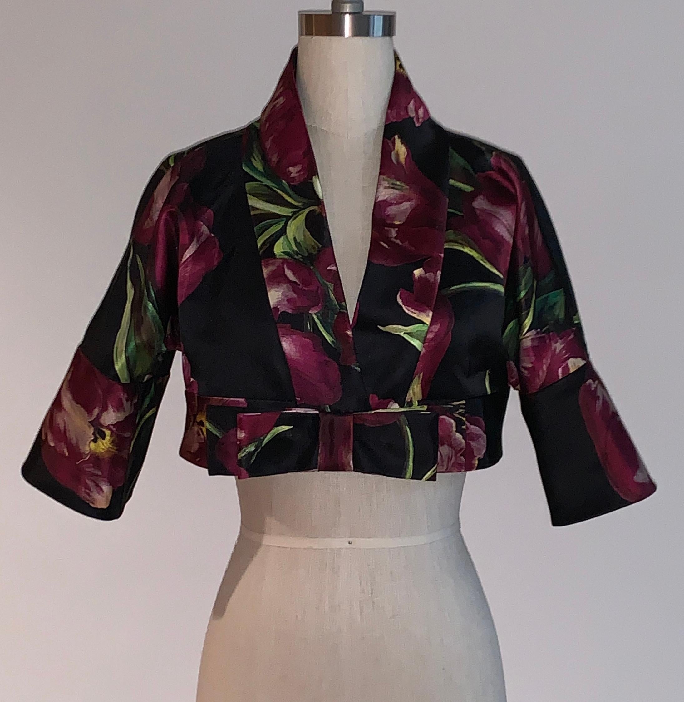 Dolce & Gabbana black and purplish floral tulip print silk cropped bolero with bow detail at front, wide sleeves. Fastens at front with two hidden snap closures. 

100% silk.
Lined in 100% silk.

Made in Italy.

Size IT 38, approximate US 2. See