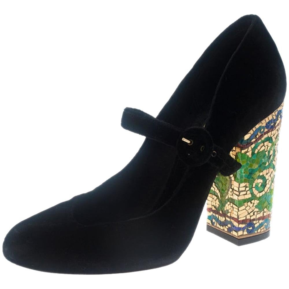 These Dolce and Gabbana Mary Jane Pumps will add character to any outfit! Made from soft black colored velvet, they feature straps across their vamps. They have chunky 11cm heels that are embellished with colorful mosaic-like designs. Lined with