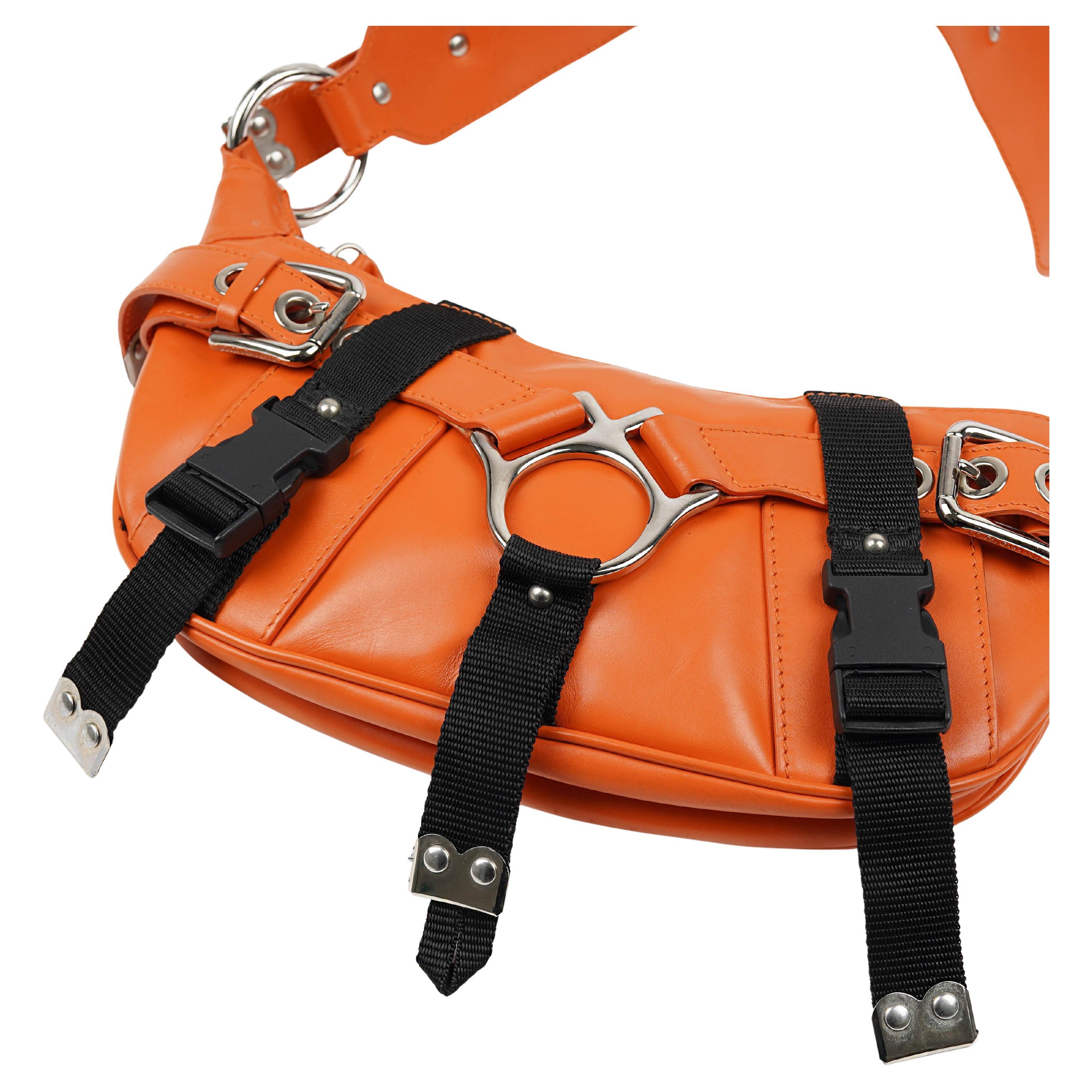 Rare sac à bandoulière Dolce & Gabbana inspiré du bondage, issu de la collection automne/hiver 2003, réalisé en cuir orange vif et contrasté par des sangles noires et des ferrures argentées surdimensionnées. Le modèle présente une silhouette