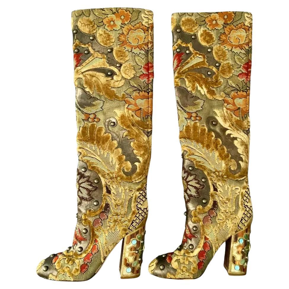 Dolce & Gabbana's Multicolor Brocade Fabric Over The Knee Boots boast a striking combination of beige velvet, brown leather, and intricate embellishments like stones and studs. The heel is adorned with artisanal wooden details, atop a leather