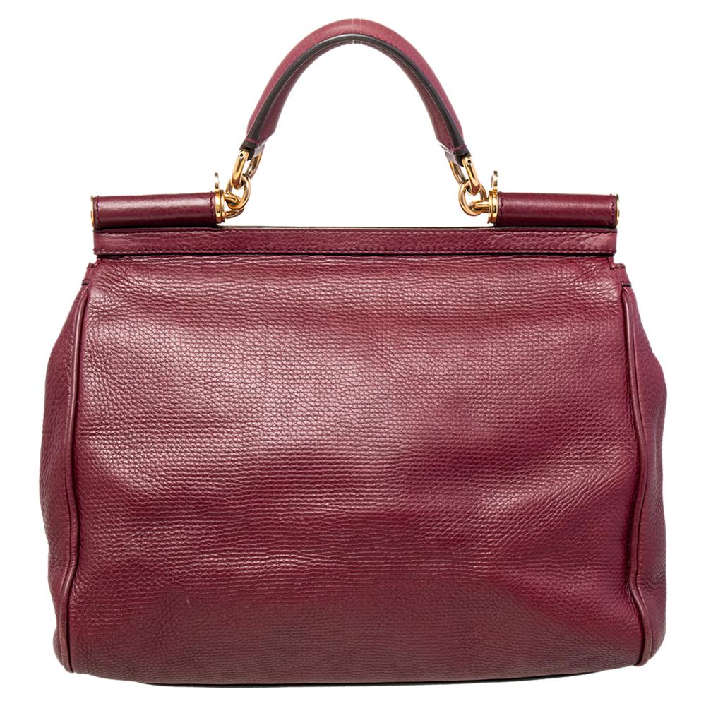 This burgundy Miss Sicily leather bag from Dolce & Gabbana has a flap that opens to a compartment with fabric lining and enough space to fit your essentials. It comes with gold-tone hardware, a top handle, and the brand plaque at the front. Complete