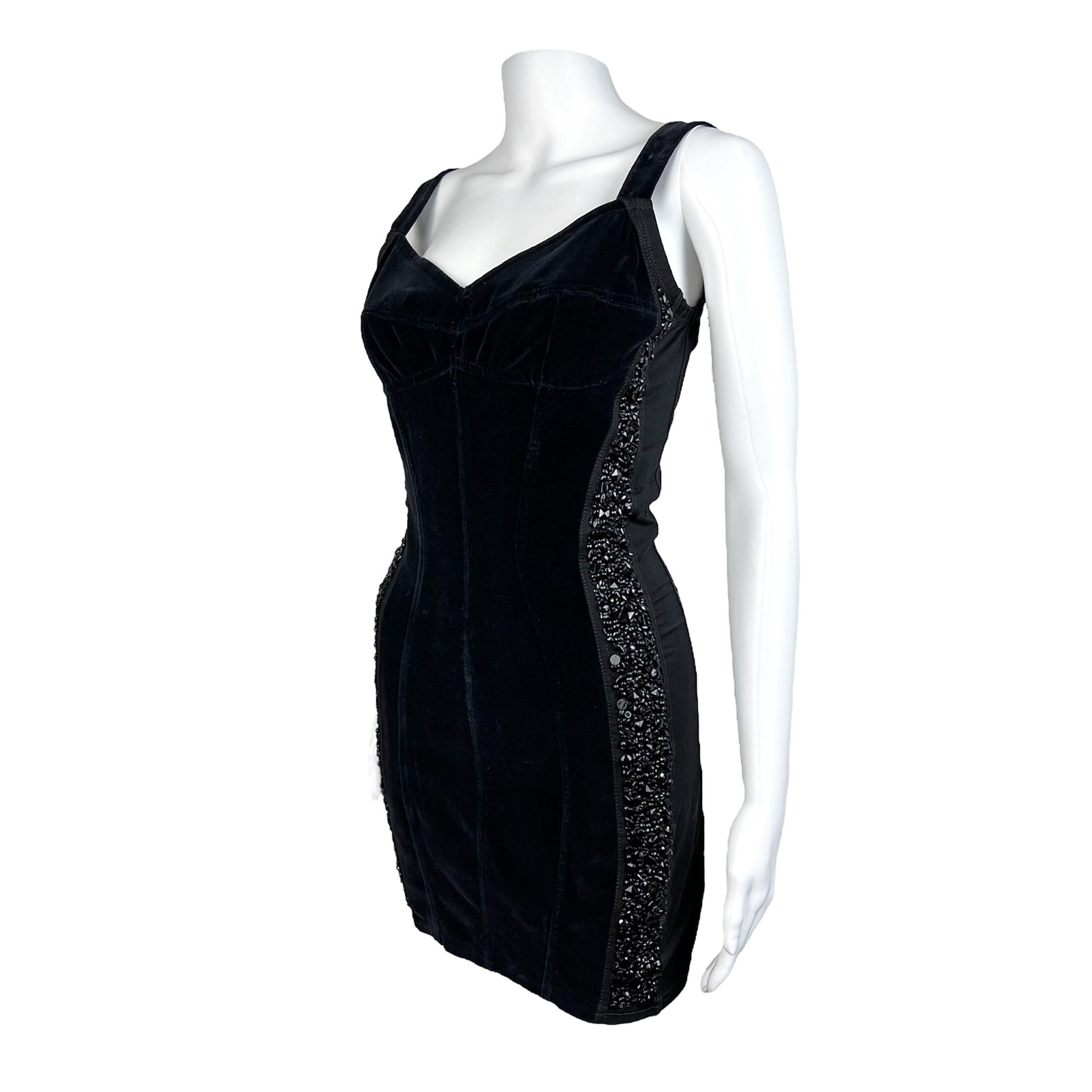 Super süßes schwarzes Minikleid von Dolce & Gabbana aus den frühen 90ern mit Kristalleinsätzen an beiden Seiten. Das Kleid ist aus einem schönen Samt und dehnbaren Einsätzen gefertigt. Die Form ist körperbetont und ist direkt von Dessous und