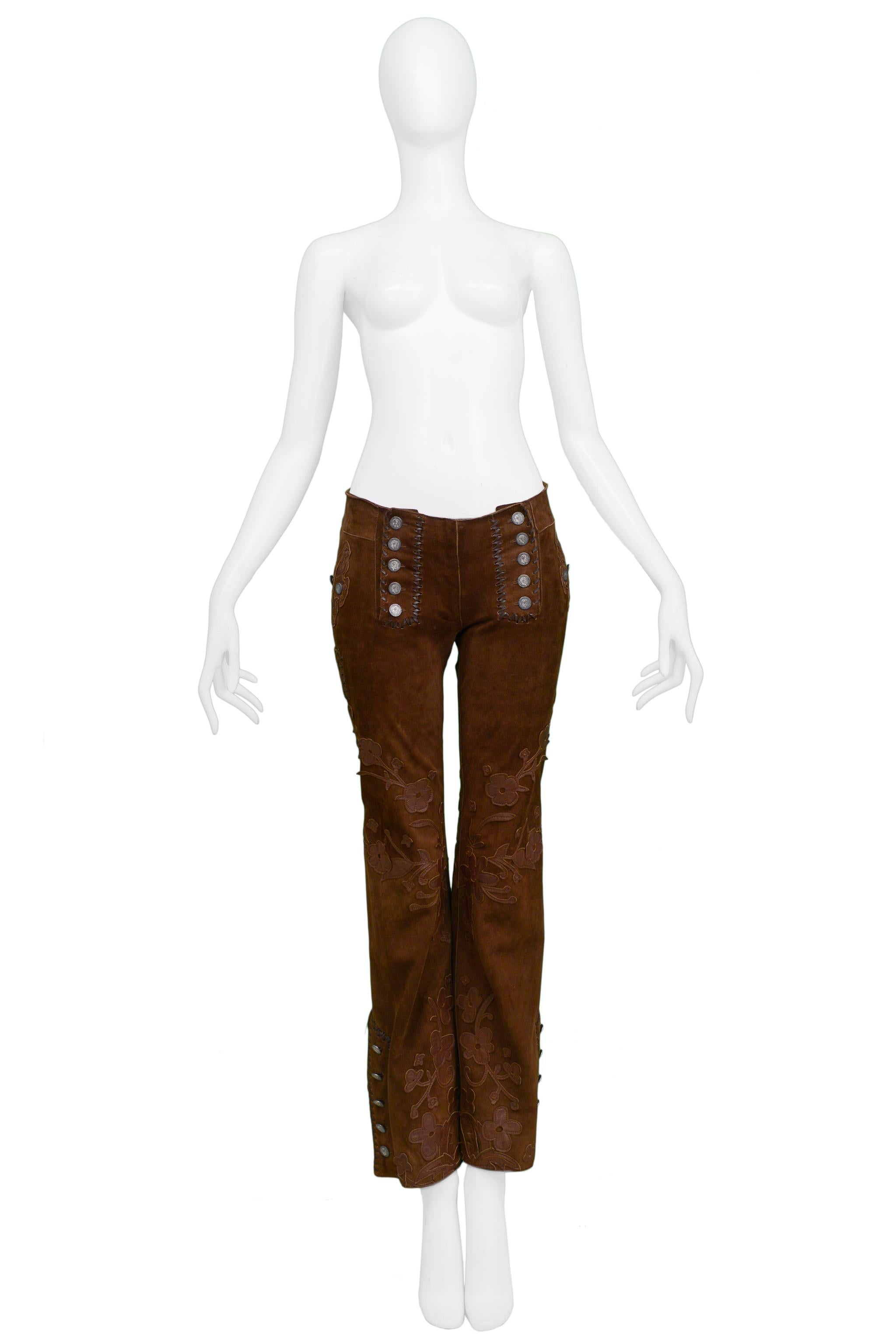 Resurrection Vintage is excited to offer a vintage Dolce & Gabbana brown suede leather pants featuring brown leather floral appliques, whipstitching, button front yoke, brass buckle back belt, back pocket flaps, and flared legs with buttons on the
