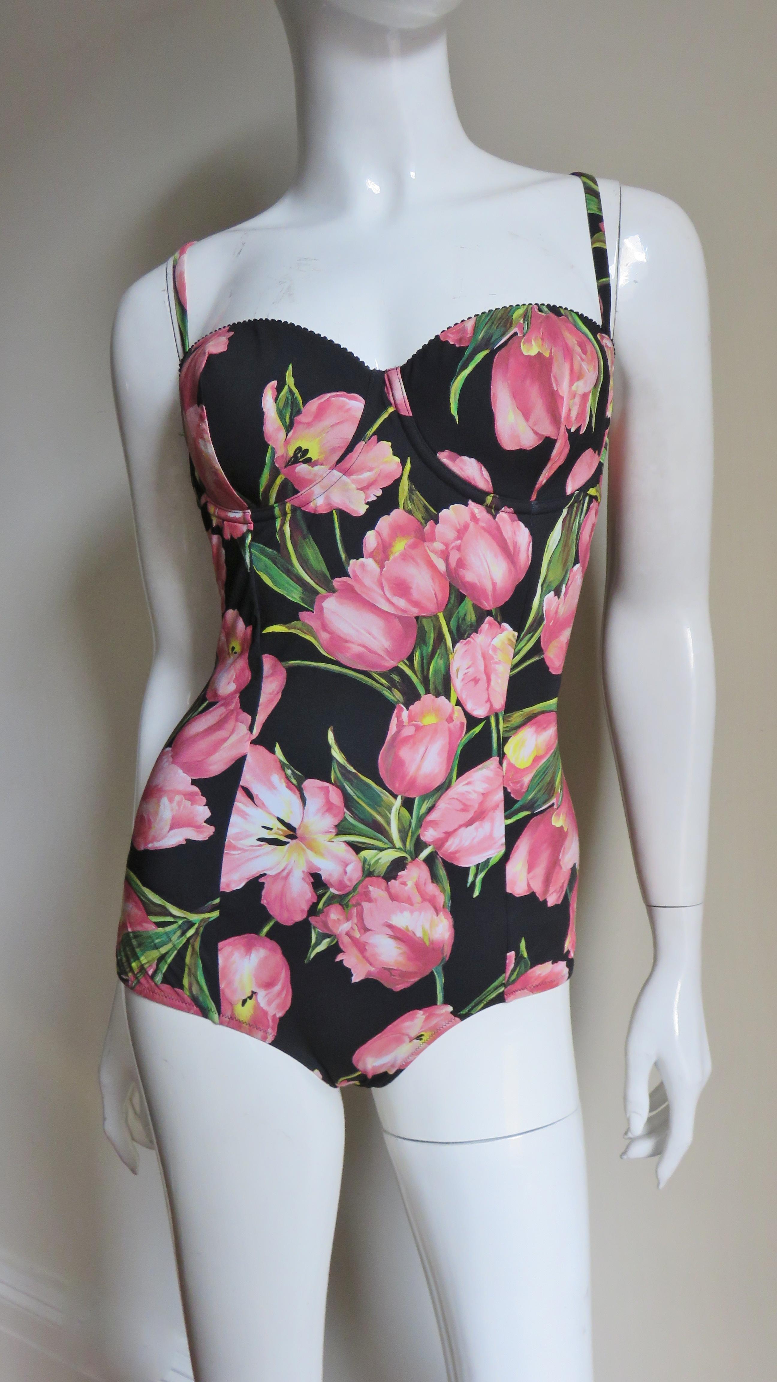 A beautiful one piece swimsuit from Dolce and Gabbana with pink and green tulips on a black background.  It has small straps which can be removed to wear the suit strapless, molded underwire bust cups and a longer line on the leg.  It closes in the