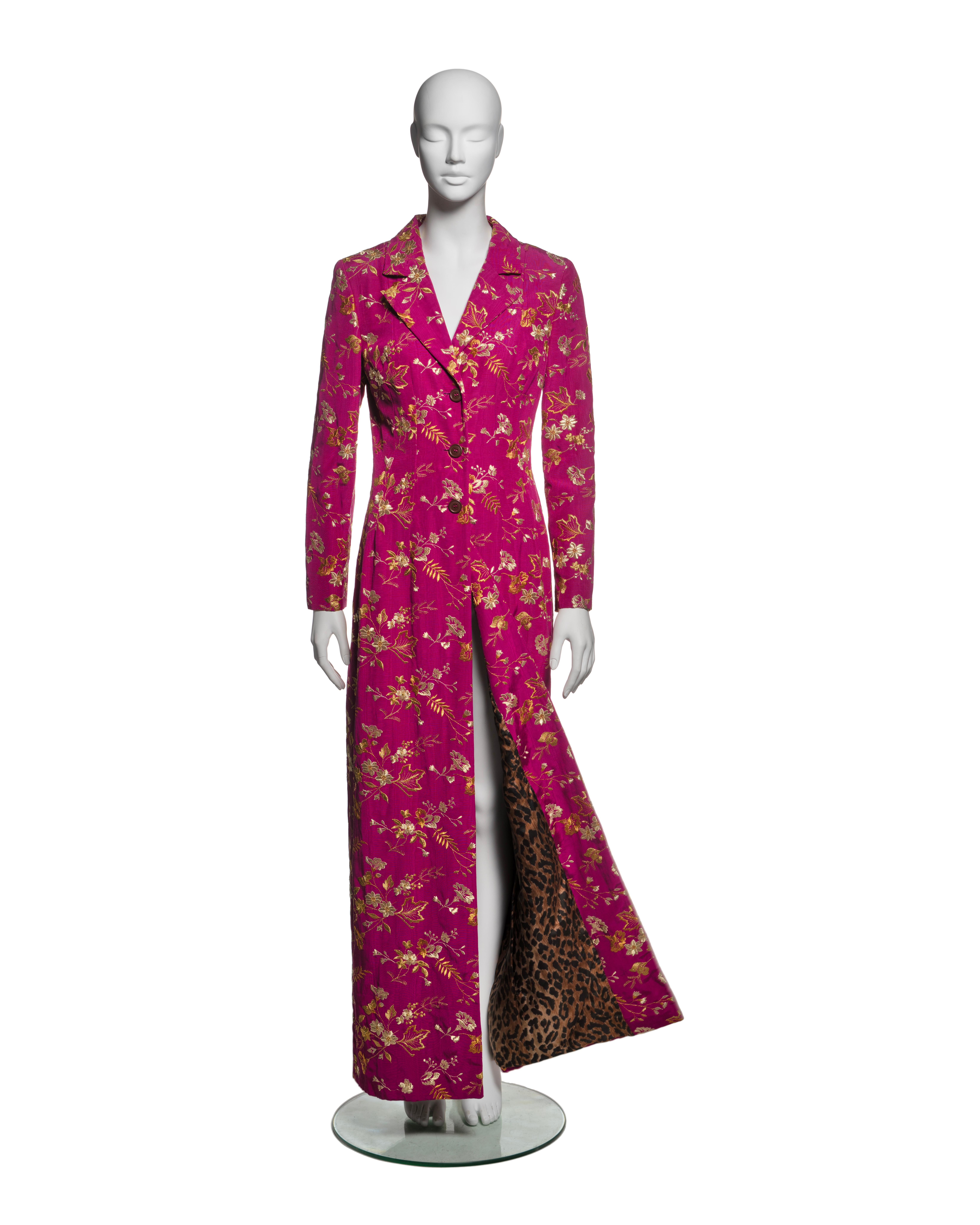 This Dolce & Gabbana Fall-Winter 1997 collection dress coat is crafted from magenta moiré fabric and features fully embroidered floral motifs gold and amber tones. The design showcases a structured silhouette with a notched lapel collar, long