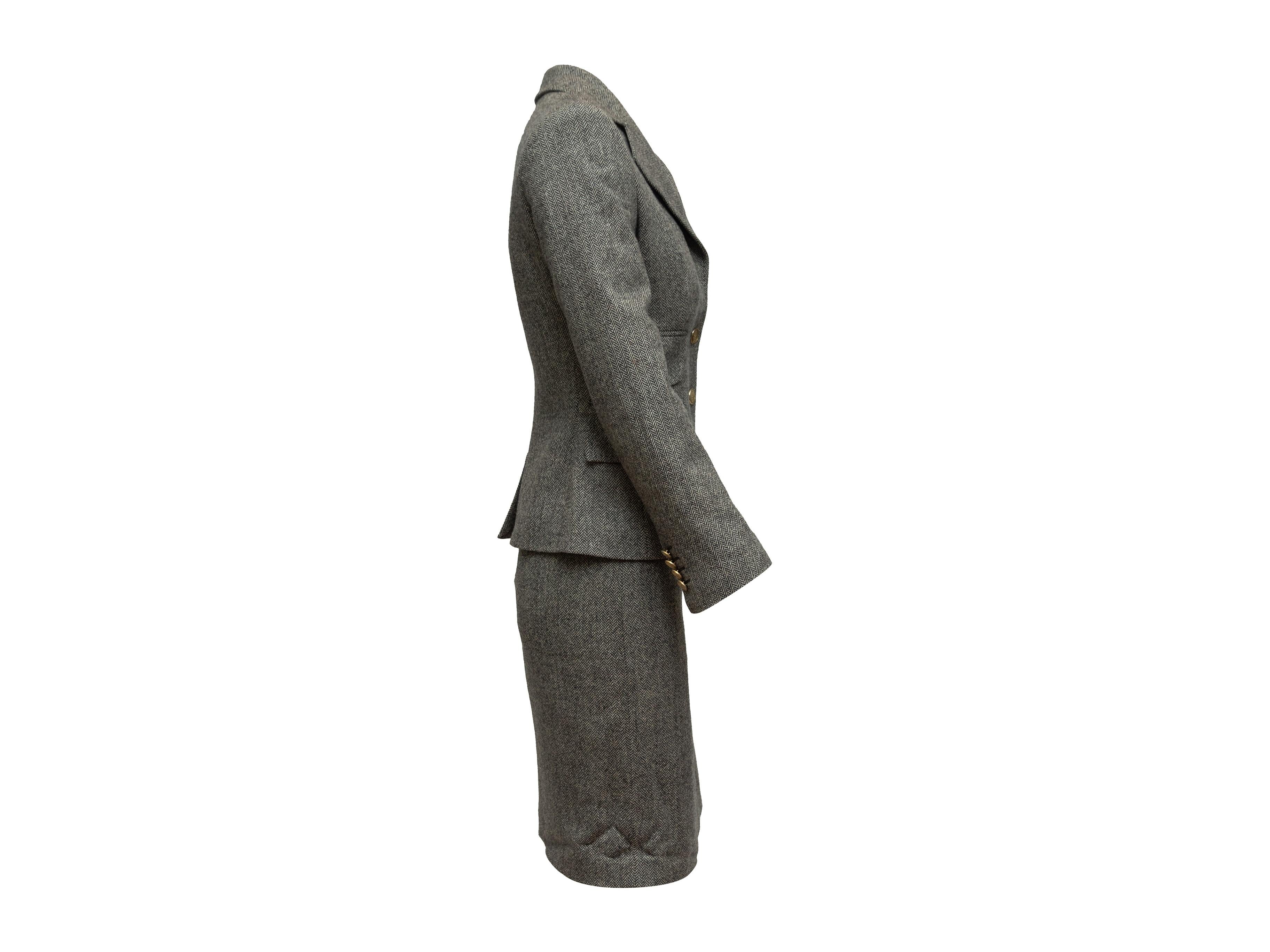 Product details: Grey cashmere and virgin wool skirt suit by Dolce & Gabbana. Herringbone pattern throughout. Notched lapel. Three flap pockets at blazer. Gold-tone button closures at blazer. Designer size 38. Blazer- 29