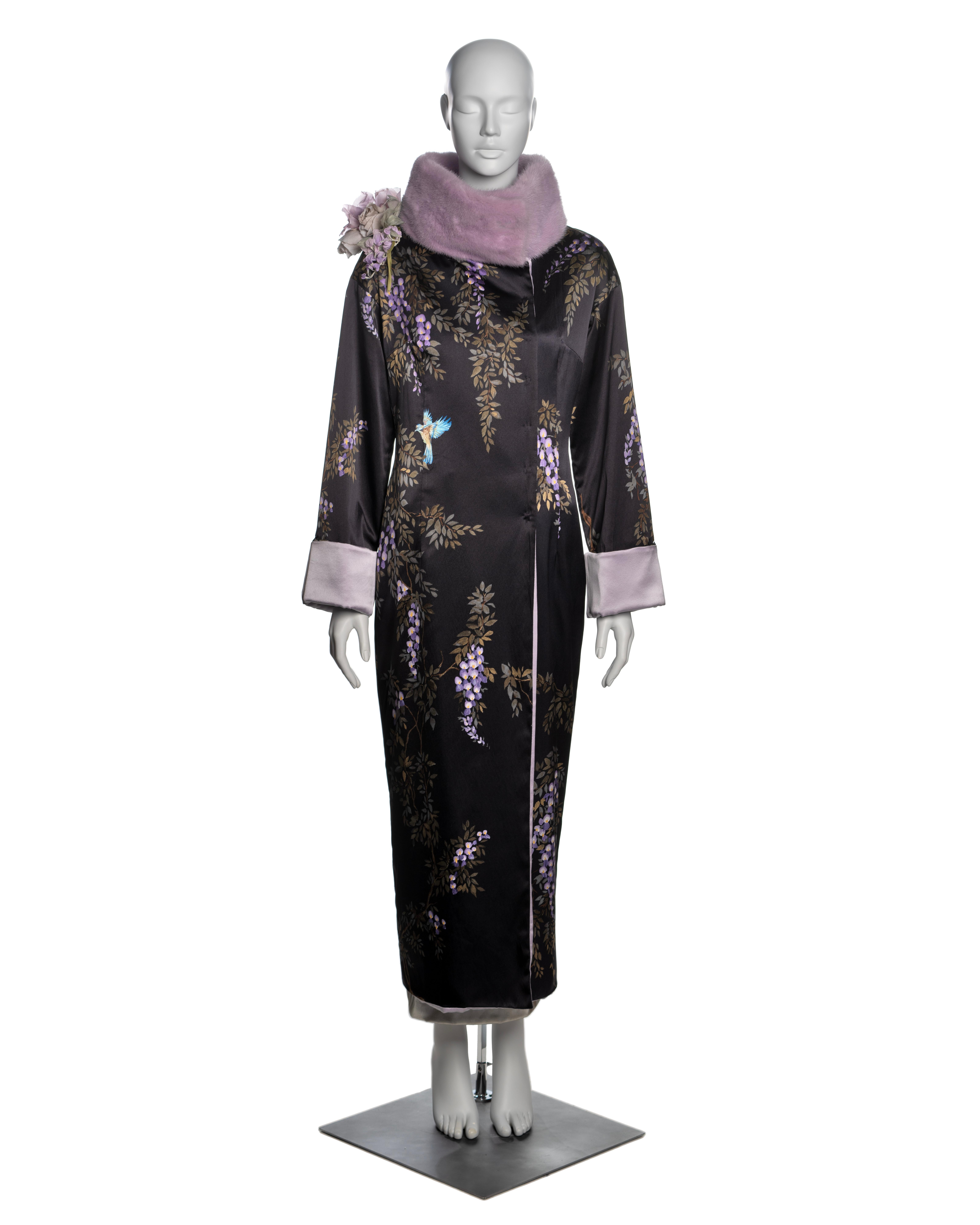 This Dolce & Gabbana evening coat is crafted from luxurious black silk, hand-painted with intricate floral designs in shades of purple and green, featuring accents of bluebirds. The coat is complemented by a lavender mink fur trim at the wide collar