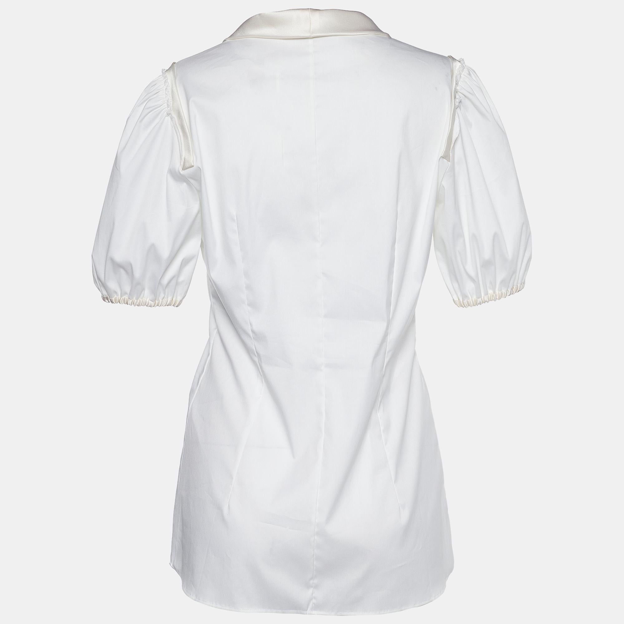 This blouse from the House of Dolce & Gabbana is a beautiful creation you need to add to your closet. It is made from off-white poplin fabric, which is elevated with a bow tie on the front. It flaunts short sleeves and buttoned closures. Style this