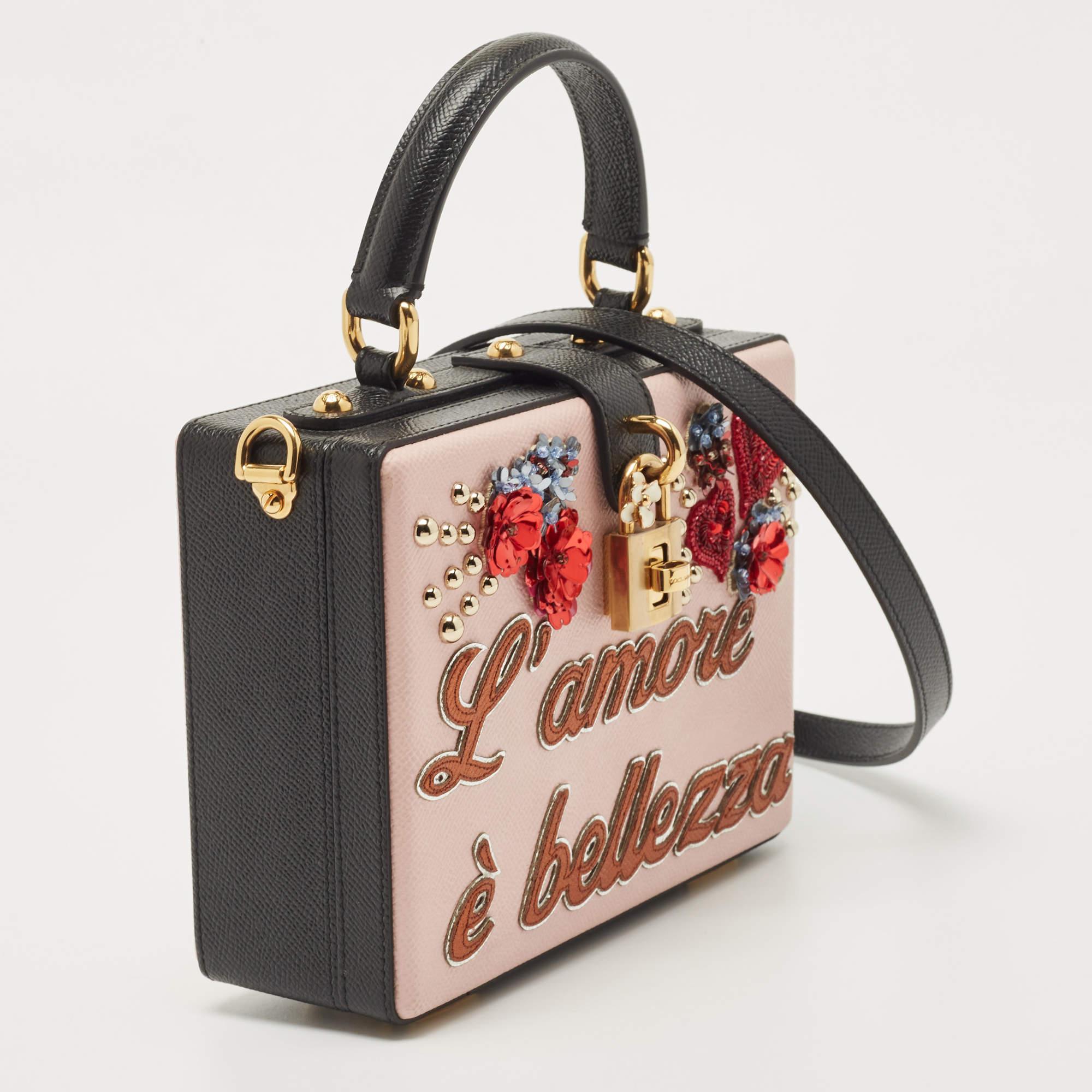 The Dolce & Gabbana L'Amore bag is a luxurious and eye-catching accessory. Crafted from premium leather, it features a vibrant pink and black color scheme, intricate embellishments, and a structured box design. The top handle adds a touch of