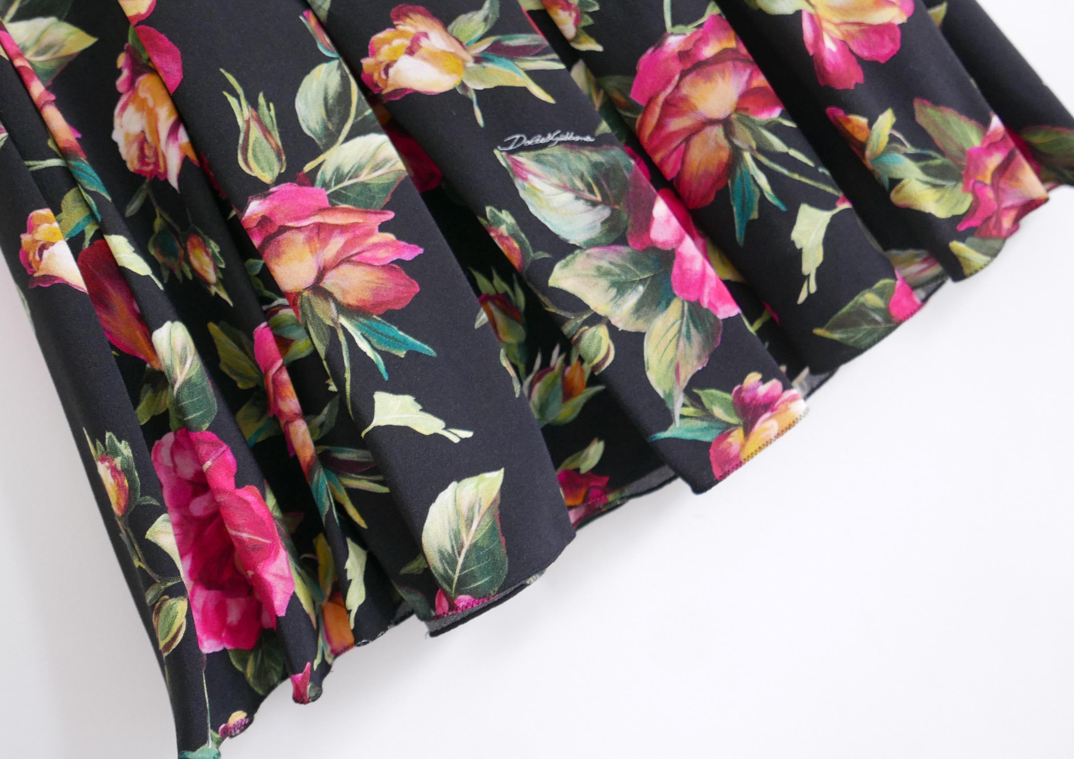Magnifique jupe plissée à imprimé rose Dolce & Gabbana. Acheté pour £950 et neuf avec étiquettes. Confectionné en crêpe de viscose imprimé de roses sauvages sur fond noir, il est entièrement doublé de soie/élasthanne. Il présente une coupe évasée