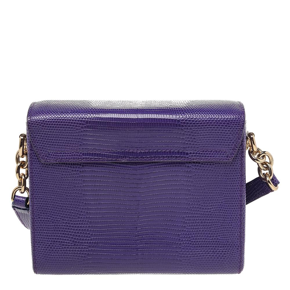This Dolce & Gabbana handbag is a must-have for the fashion-conscious. Embrace your natural style with this alluring handbag. Crafted from lizard-embossed leather, it has a lovely purple hue. The detail that catches the eye is the embellished DG