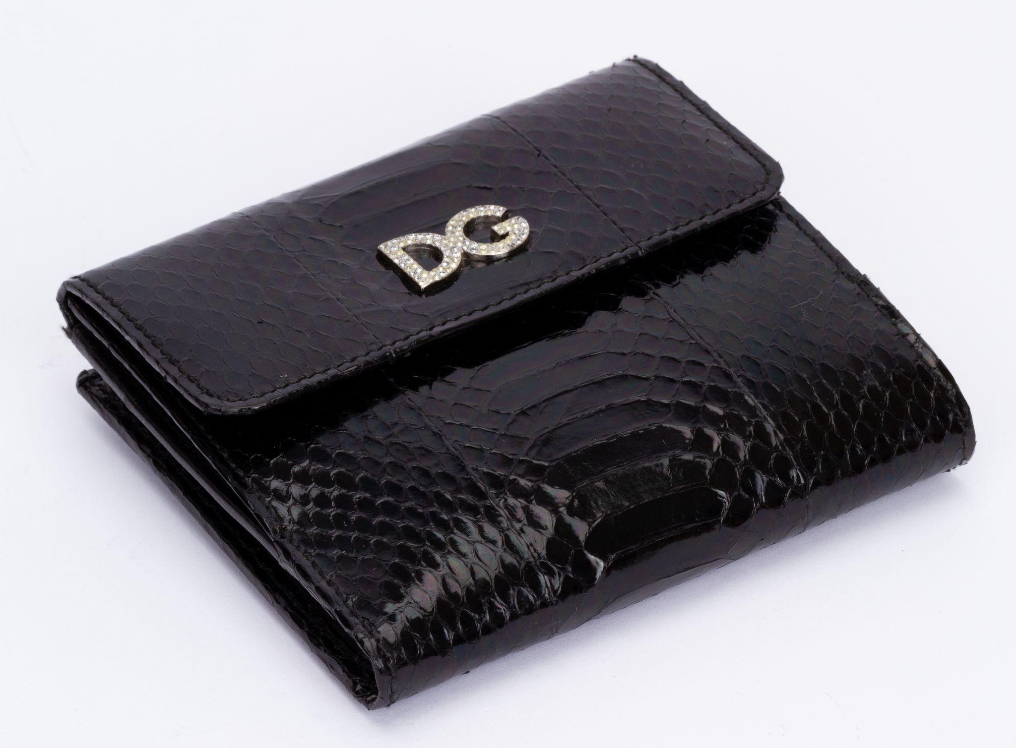 Dolce & Gabbana wallet in black made out of python skin. On the front is a DG logo featuring small crystals. It closes with a press button. The inside is decorated with severals card holders and a zipped pocket as well as part for money. It is brand
