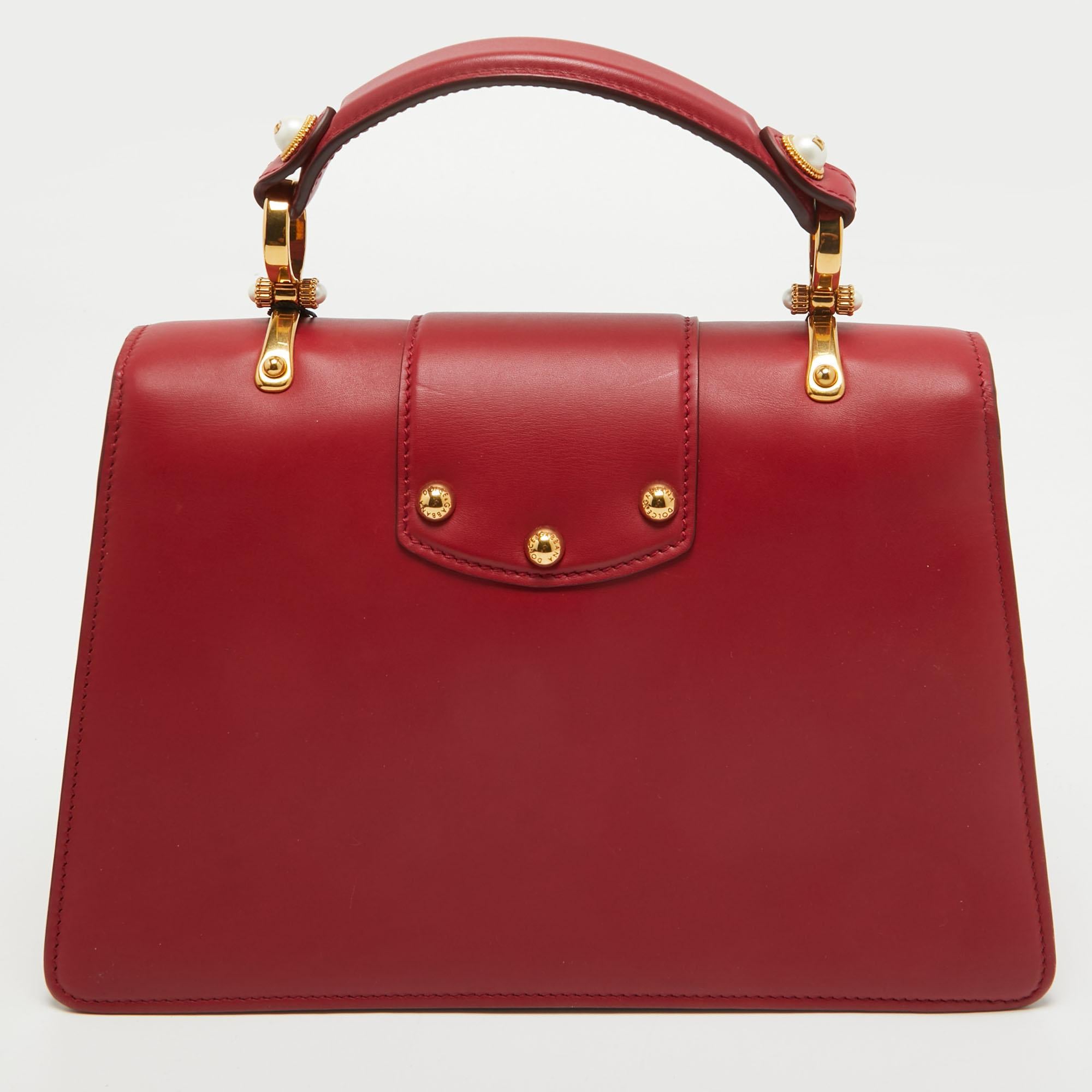 Bien structuré et très stylé, ce sac DG Amore de Dolce & Gabbana mérite d'être le vôtre ! Confectionné en cuir rouge, il est doté d'une poignée supérieure et d'une bandoulière amovible. Il est également doté d'un logo embelli en tons dorés sur le