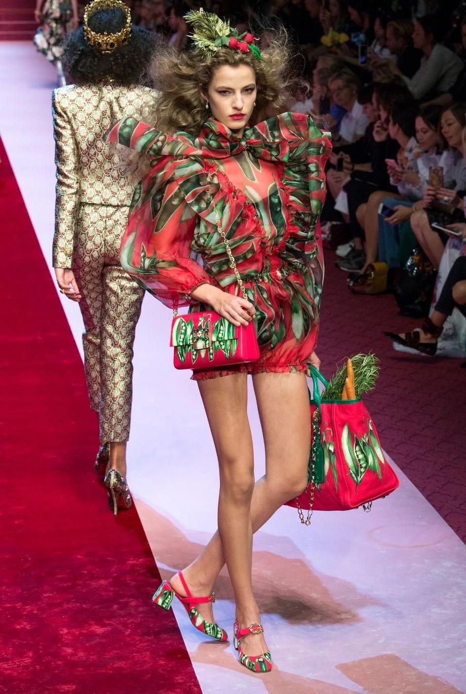 Resurrection Vintage è entusiasta di offrire una tutina floreale in organza rossa con volant di Dolce & Gabbana del 2018. Il pagliaccetto presenta un collo a cravatta, pantaloncini in stile bloomer e una chiusura posteriore con zip nascosta. 
Dolce