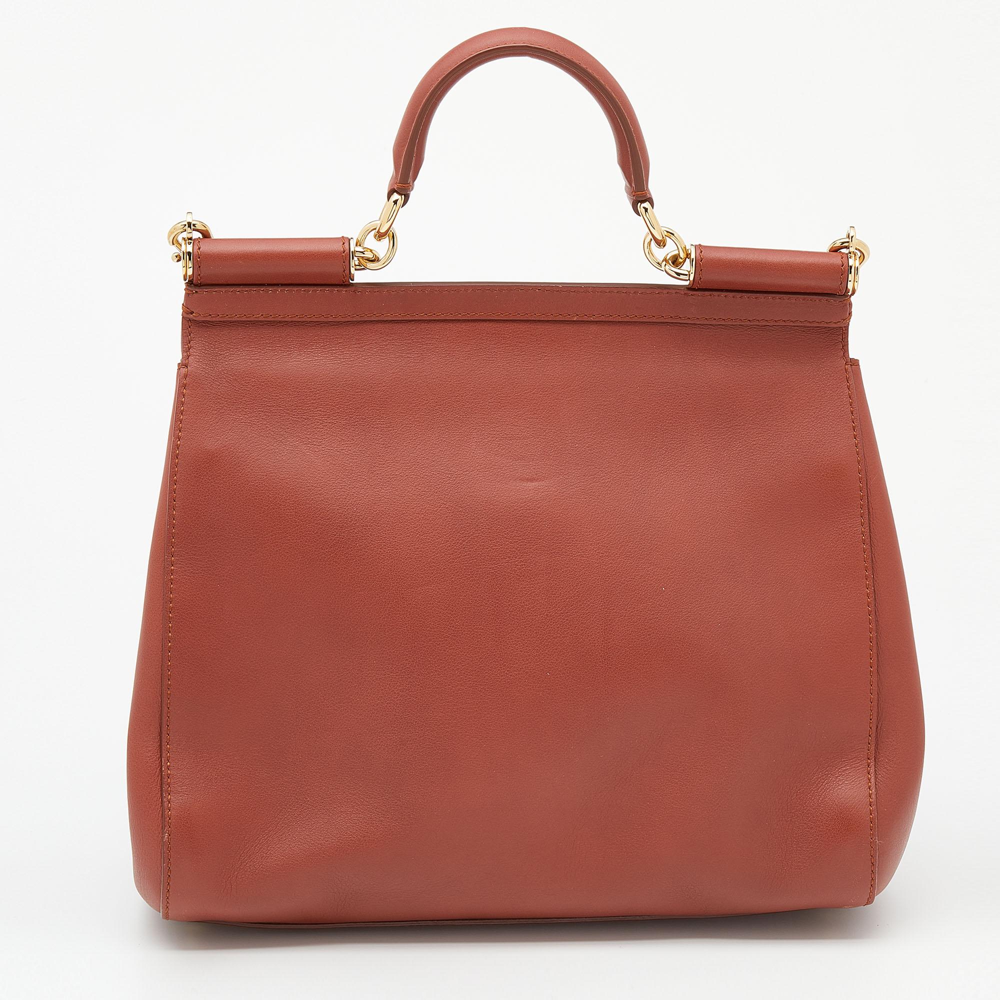Meticulously crafted into an eye-catchy shape, this Miss Sicily bag from the House of Dolce & Gabbana exudes just the right amount of charm and elegance! It is made from rust-orange leather, with a gold-toned logo plaque accentuating the front. It