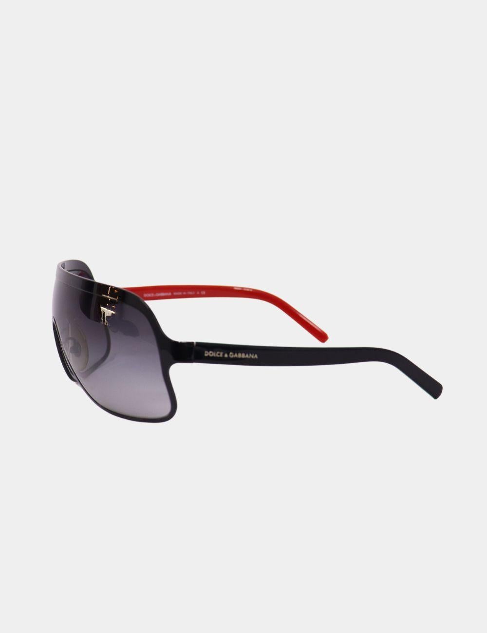 Turn heads with these bold and modern Dolce & Gabbana shield sunglasses. Featuring a sleek wraparound visor-style lens with gradient tint, these sunglasses are accented with a striking contrast design—black front frame with red temple arms. Designed
