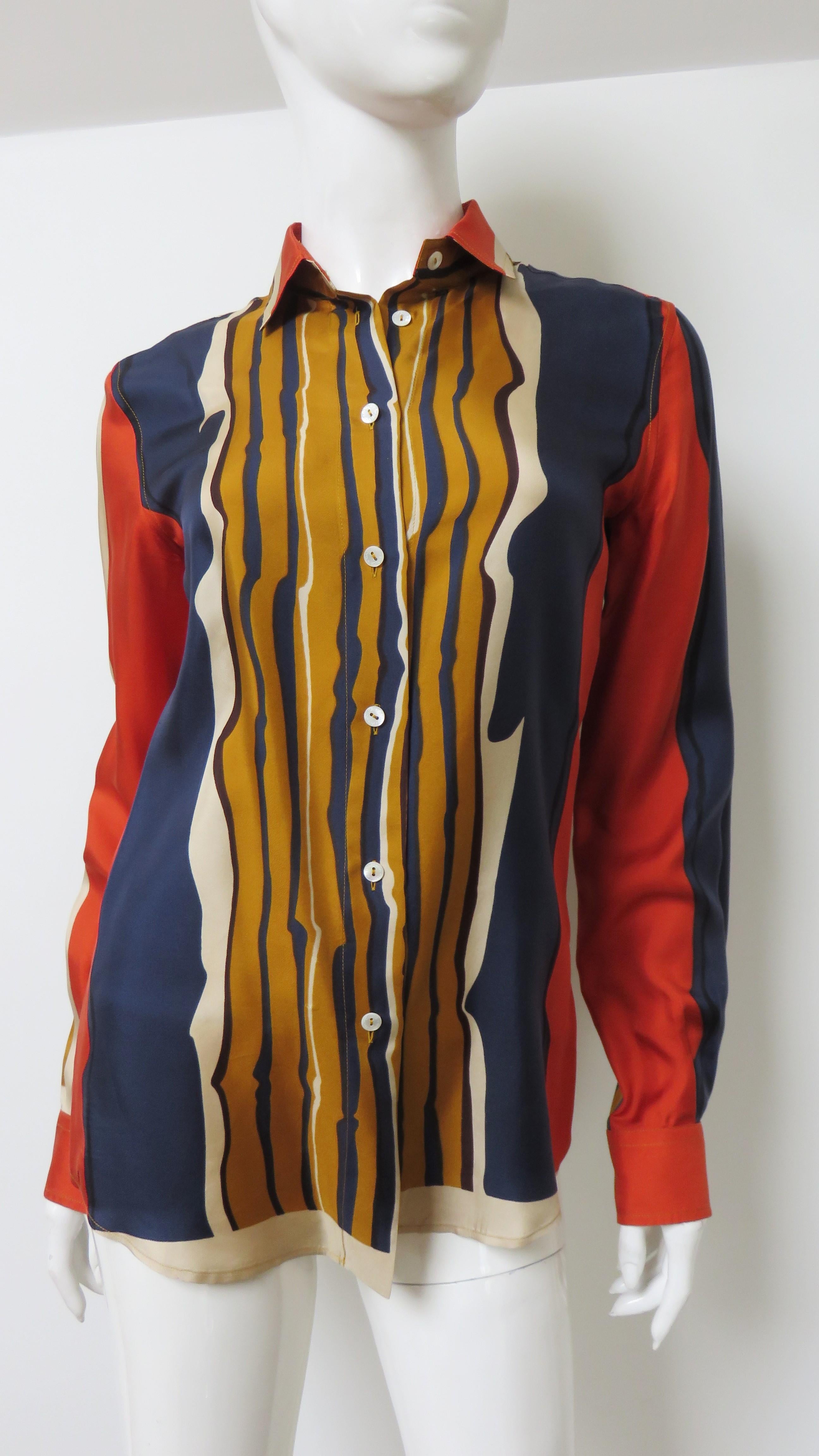 Una bellissima camicia di seta con un colorato motivo a righe verticali astratte in oro, arancione, blu e bianco sporco.  Ha un colletto a camicia, maniche lunghe con polsini a bottone e bottoni anteriori in madreperla con la scritta Dolce &