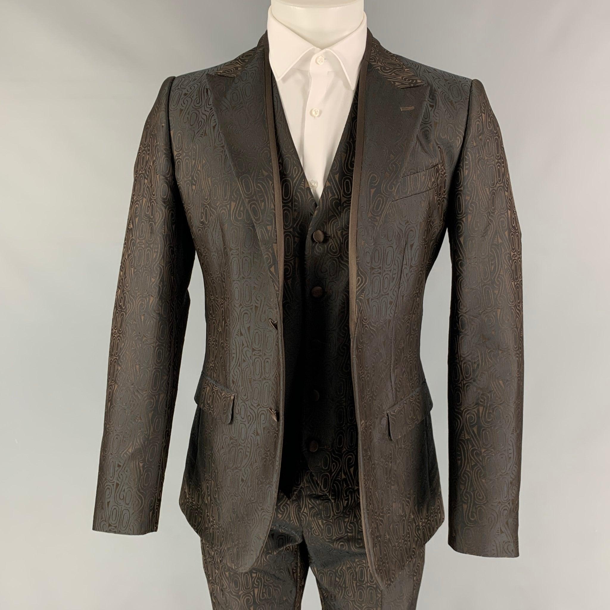 DOLCE & GABBANA 3 Piece
suit comes in a brown geometric polyester / silk with a full liner and includes a single breasted, double button sport coat with a peak lapel and matching flat front trousers. Waist and length of pants need to be altered to