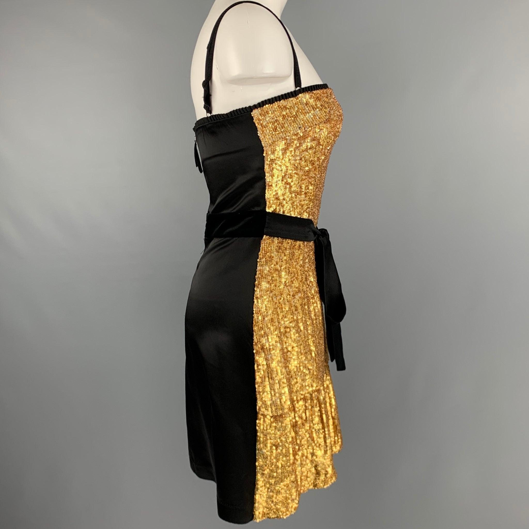 D&G by DOLCE & GABBANA cocktail dress
in a black polyester blend fabric featuring gold tone sequined front, black satin tie belt, spaghetti straps, and a back zipper closure.Very Good Pre-Owned Condition with Tags. Minor signs of wear. 

Marked:  40
