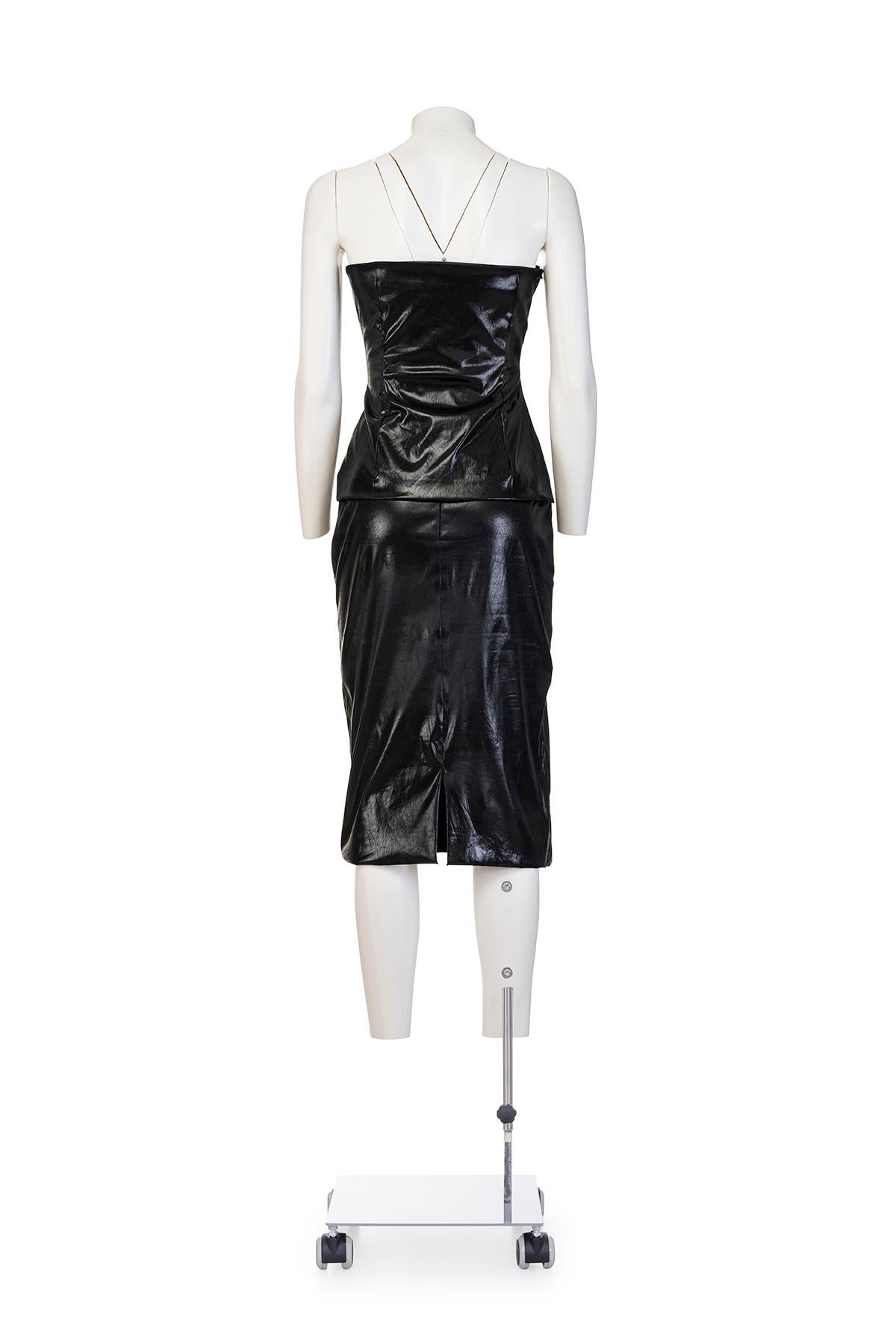 Traje entallado efecto vinilo primavera verano 1998 de Dolce & Gabbana.
Top sin tirantes con abertura lateral y cremallera.
Falda lápiz con cierre de cremallera.
Totalmente forrado.
La composición es 92% poliéster, 6% poliuretano y 2% elastano.
Las