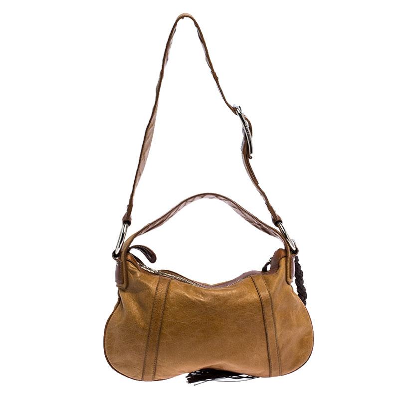 Coming from the house of Dolce and Gabbana, this bag is a dream come true for every fashionista. Crafted from tan and brown leather, the bag features a single handle, a shoulder strap and a tassel detail. The zip top closure opens to fabric lined