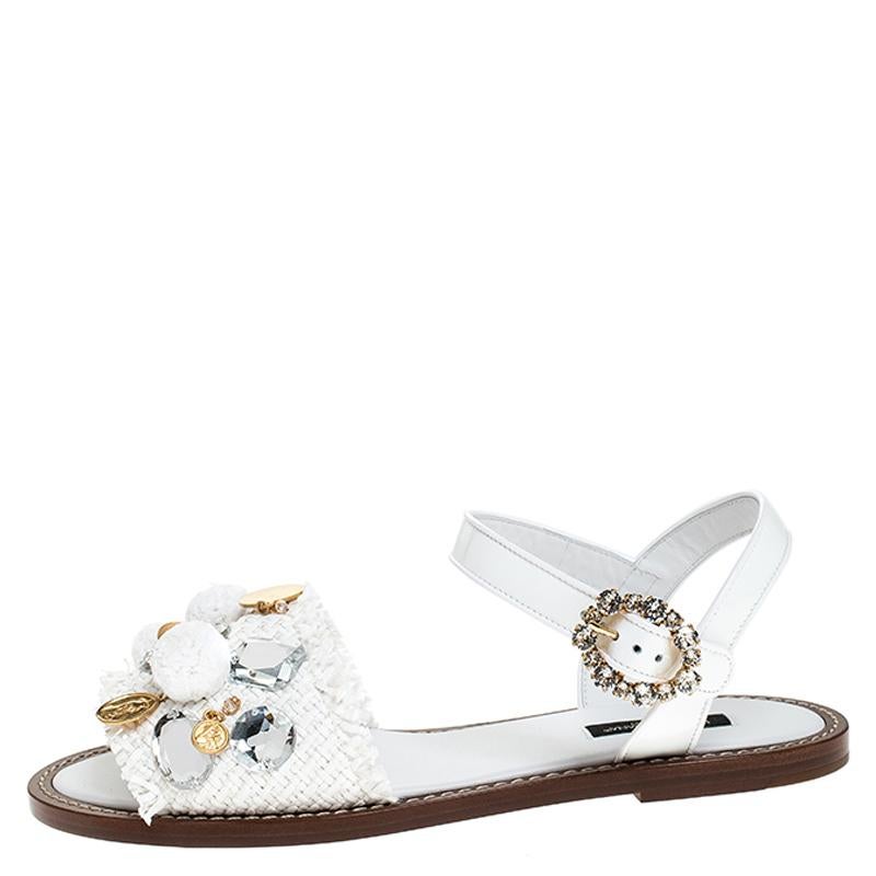 Dolce & Gabbana never fails to impress and manages to win our hearts every time! These white sandals are crafted from patent leather and feature an open toe silhouette. They flaunt the raffia straps on the toes accented with pom-poms and coin