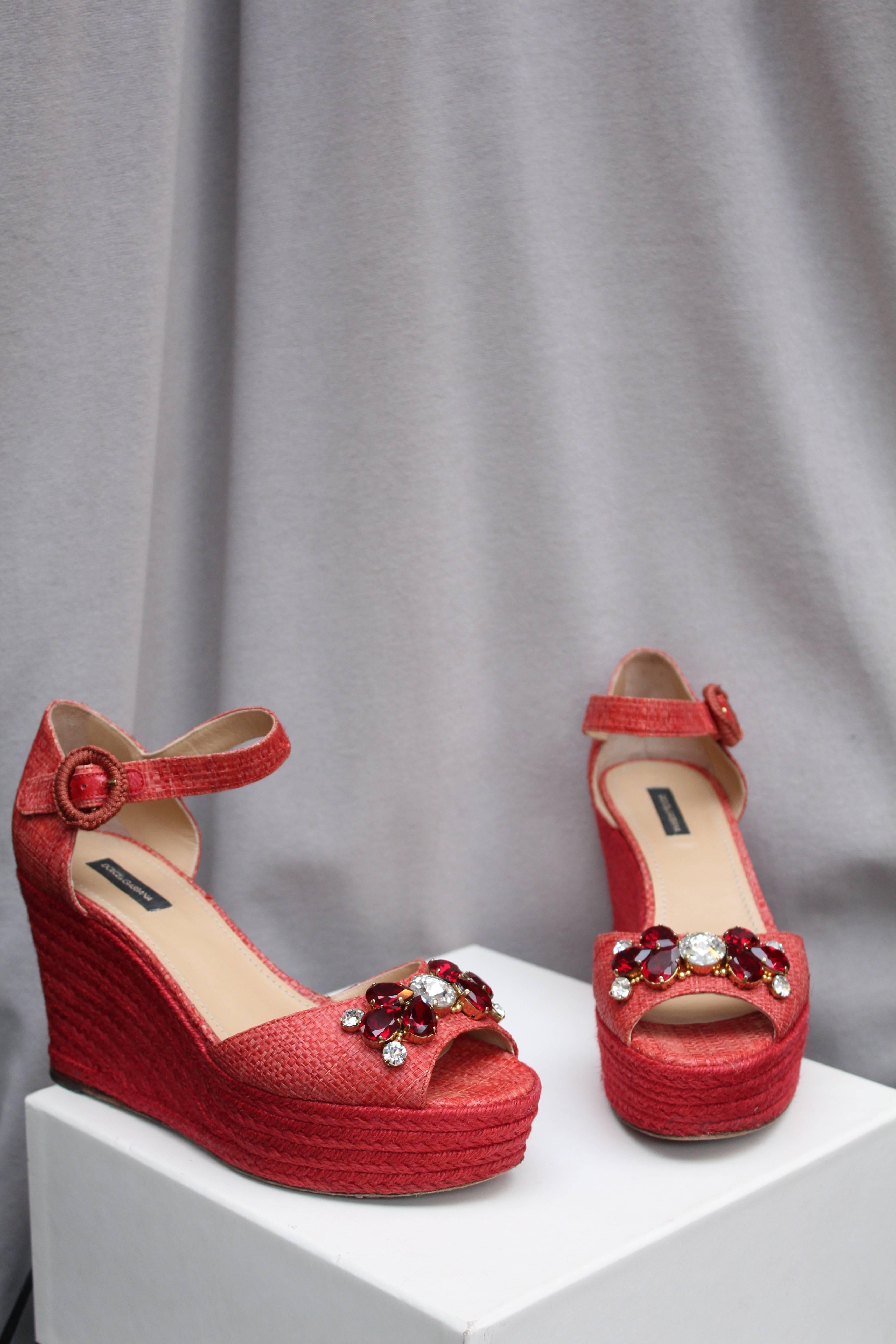 DOLCE & GABBANA (Made in Italy) Lovely platform sandals made of red raffia with woven jute sole. They are decorated in the front with faceted rhinestones in white or red colors. The gilded metal ankle strap is covered with trimmings.

This “Bianca”