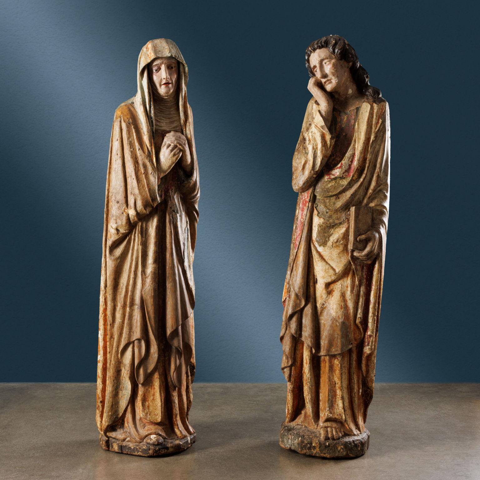 Pair of sculptures depicting the Virgin and St. John the Evangelist, portrayed in a mournful attitude. The former has a pained expression on her face, her hands clasped in front of her chest. She wears a long tunic topped with a mantle that also