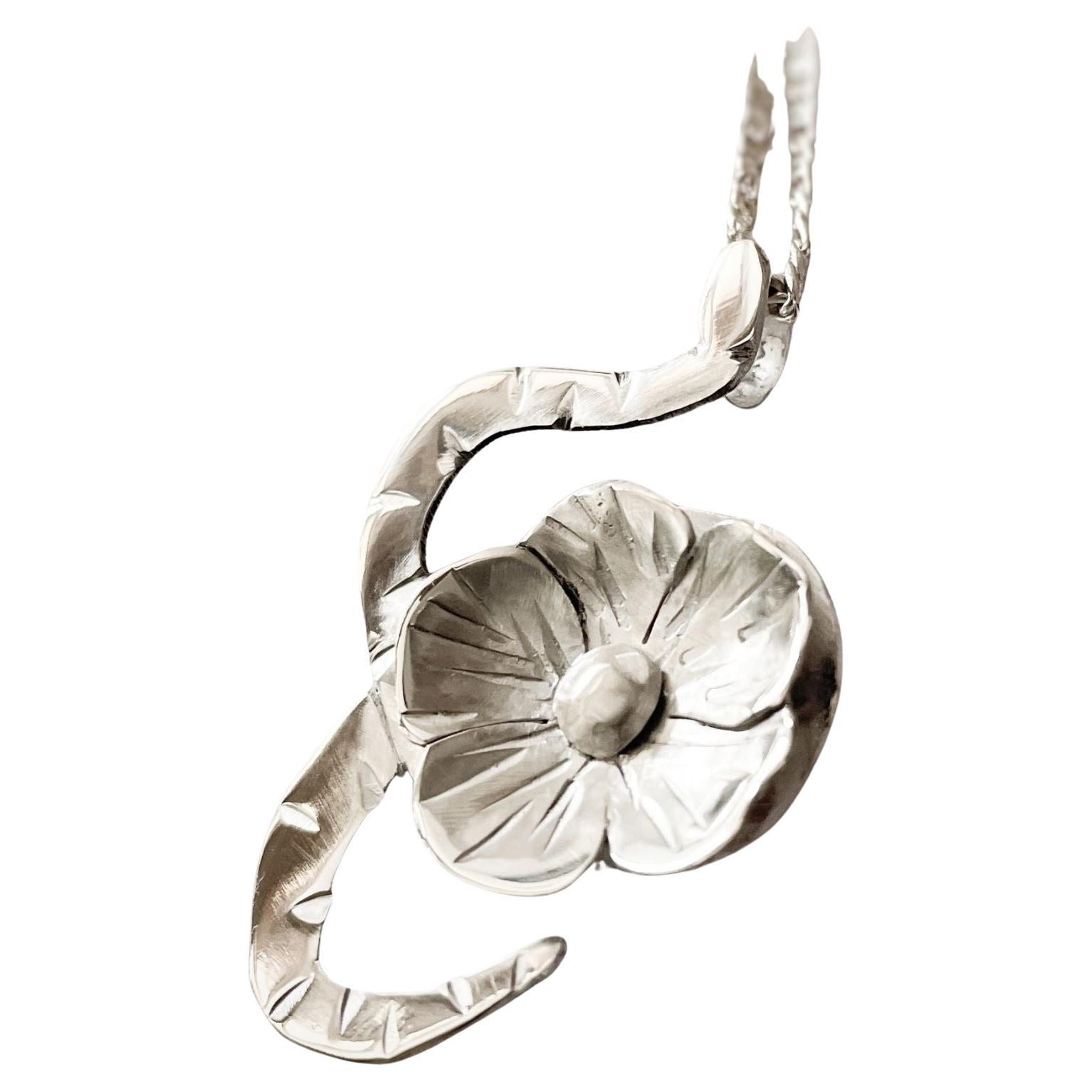 This large handcrafted pendant by Dolores Ortega features a coiled snake embracing a flower in bold relief, symbolizing the unity of strength and beauty, transformation and growth. The generous size of the pendant allows the sculptural details to