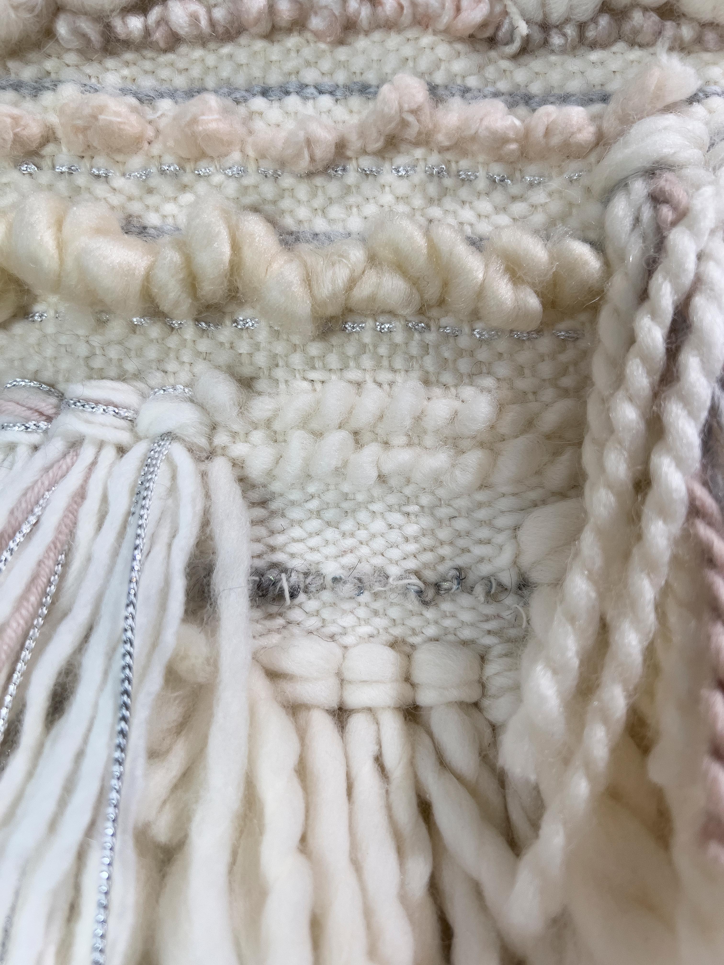 Este tapiz tejido a mano por Dolores Tema está hecho con algodón blanco claro y tonos crema y lana de alpaca y merino. La pieza está suspendida de una varilla de madera natural, lo que acentúa su estética orgánica

Dolores Tema estudió diseño en la