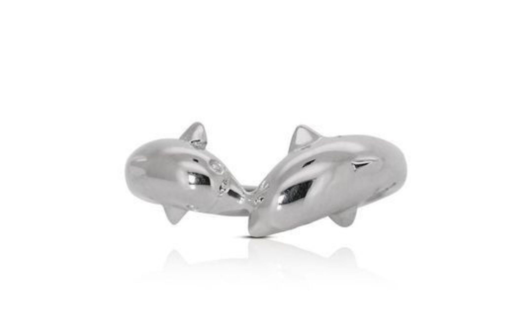 The focal point of the ring features a pair of intricately designed dolphins, crafted from lustrous 18K white gold. These dolphins seem to leap gracefully out of the ring, their sleek forms and fine details, such as their curved bodies and tails,