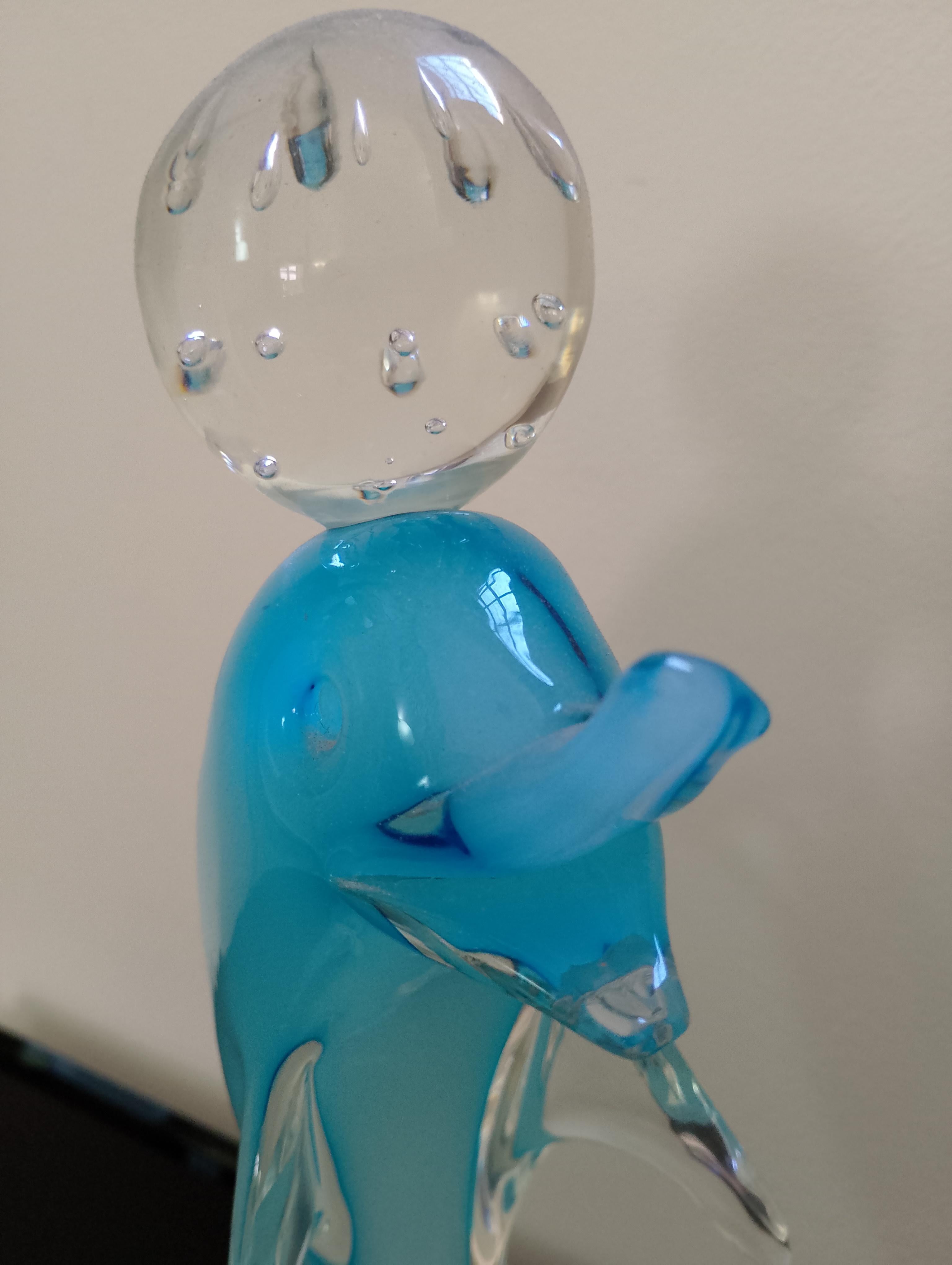 Delfino in vetro di Murano blu seduto sopra una sfera di vetro trasparente. 
